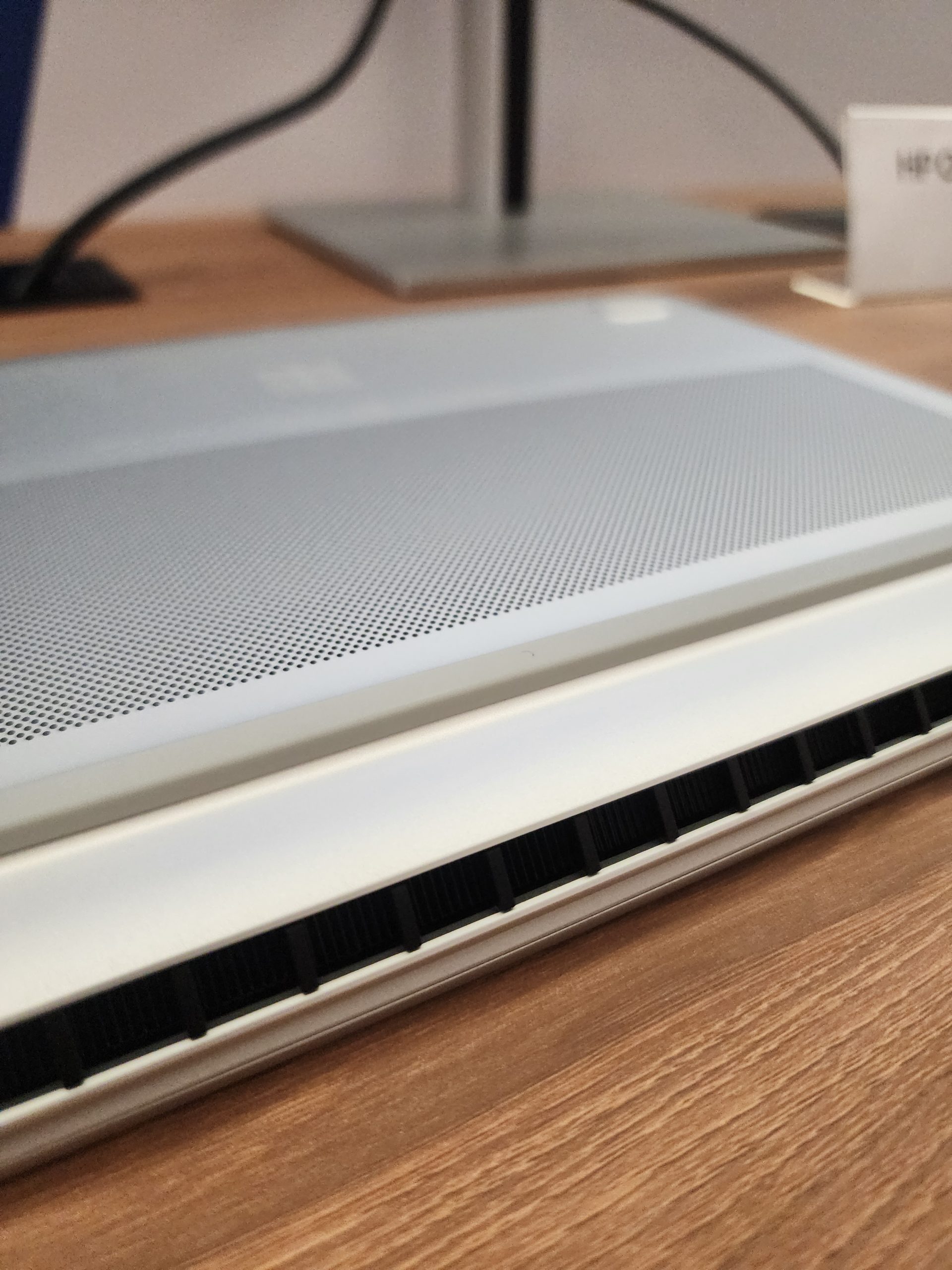 A close-up of a Dell laptop's rear vent design, showcasing its perforated surface and hinge on a wooden table.