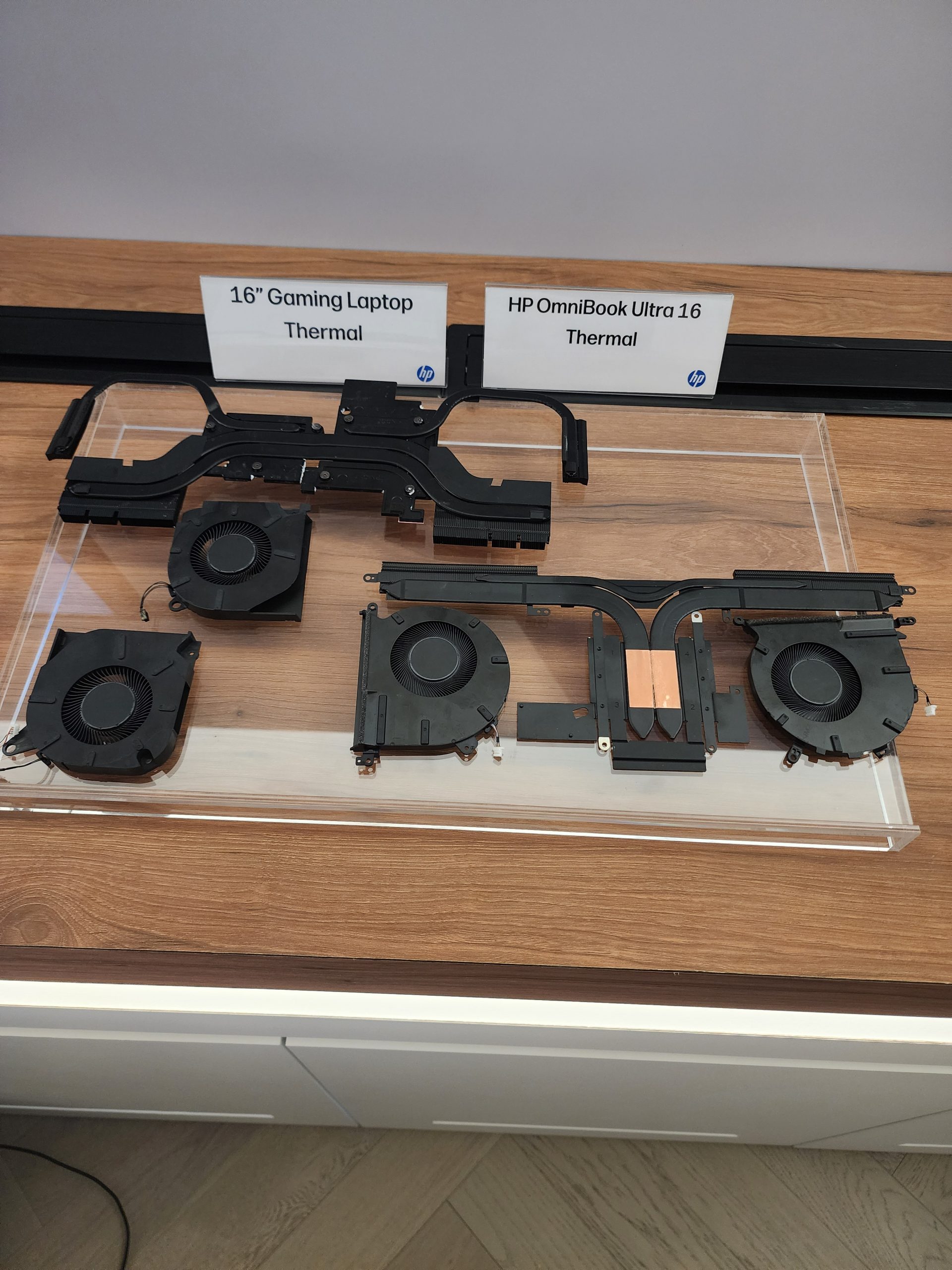 Two sets of thermal cooling components are displayed on a wooden surface with signs reading '16 Gaming Laptop Thermal' and 'HP OmniBook Ultra 16 Thermal.'