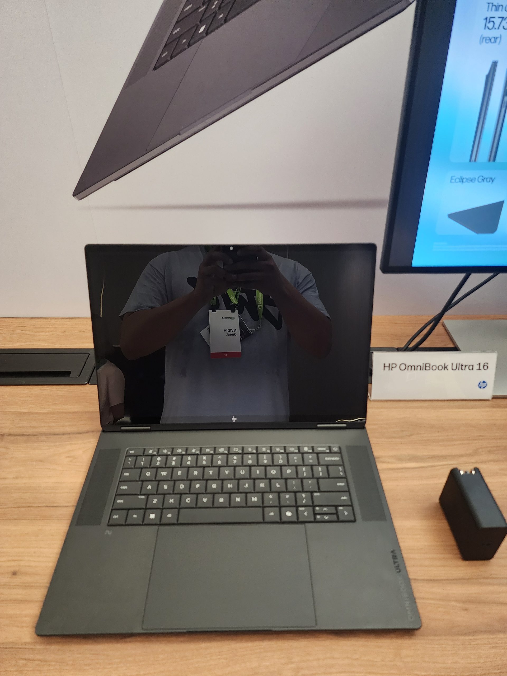 HP OmniBook Ultra 16 laptop displayed on a wooden table with a reflection of a person taking a photo on its screen.