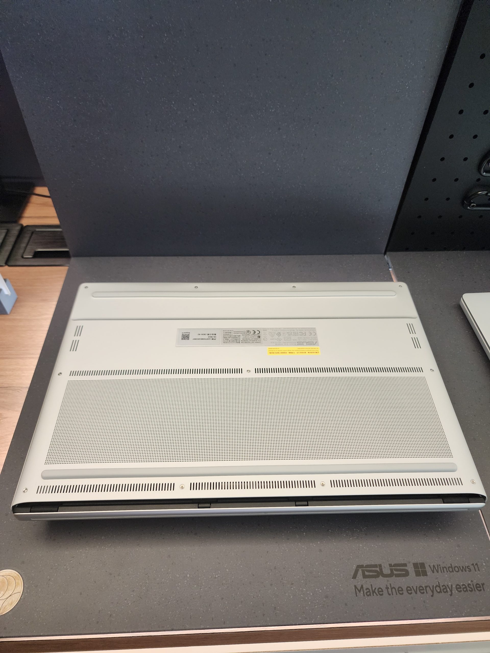 The bottom side of an ASUS laptop with multiple ventilation grills is displayed on a surface labeled 'ASUS Windows 11 Make the everyday easier'.