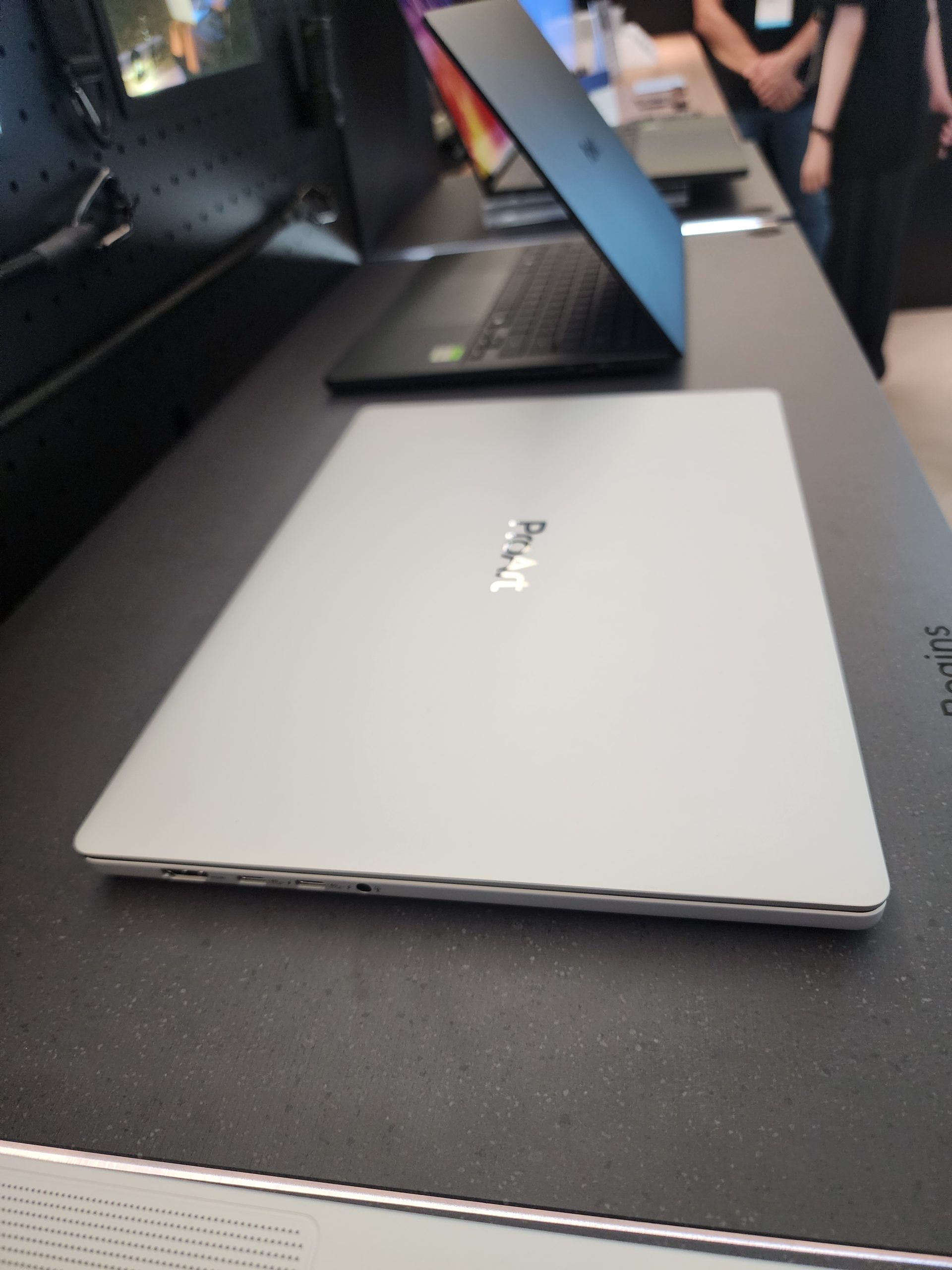 A silver ASUS ProArt laptop is displayed on a table among other laptops in a showroom setting.