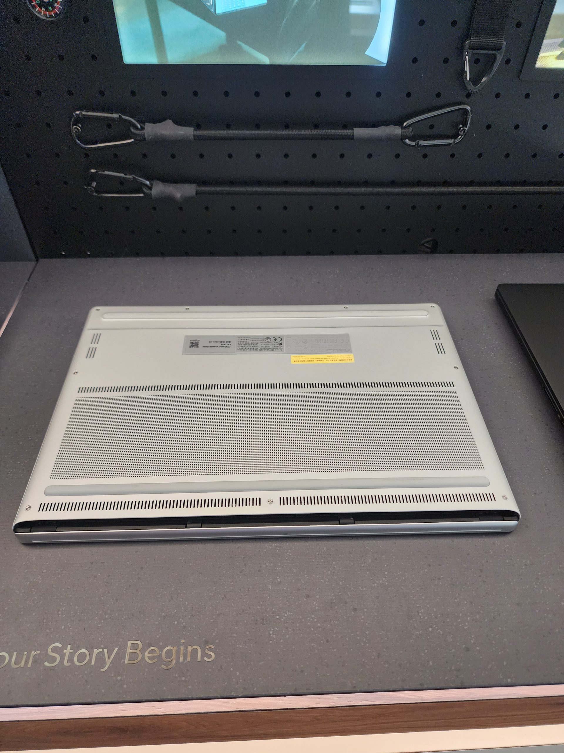 The bottom view of a silver unbranded laptop on a display surface with the words 'Your Story Begins' partially visible.