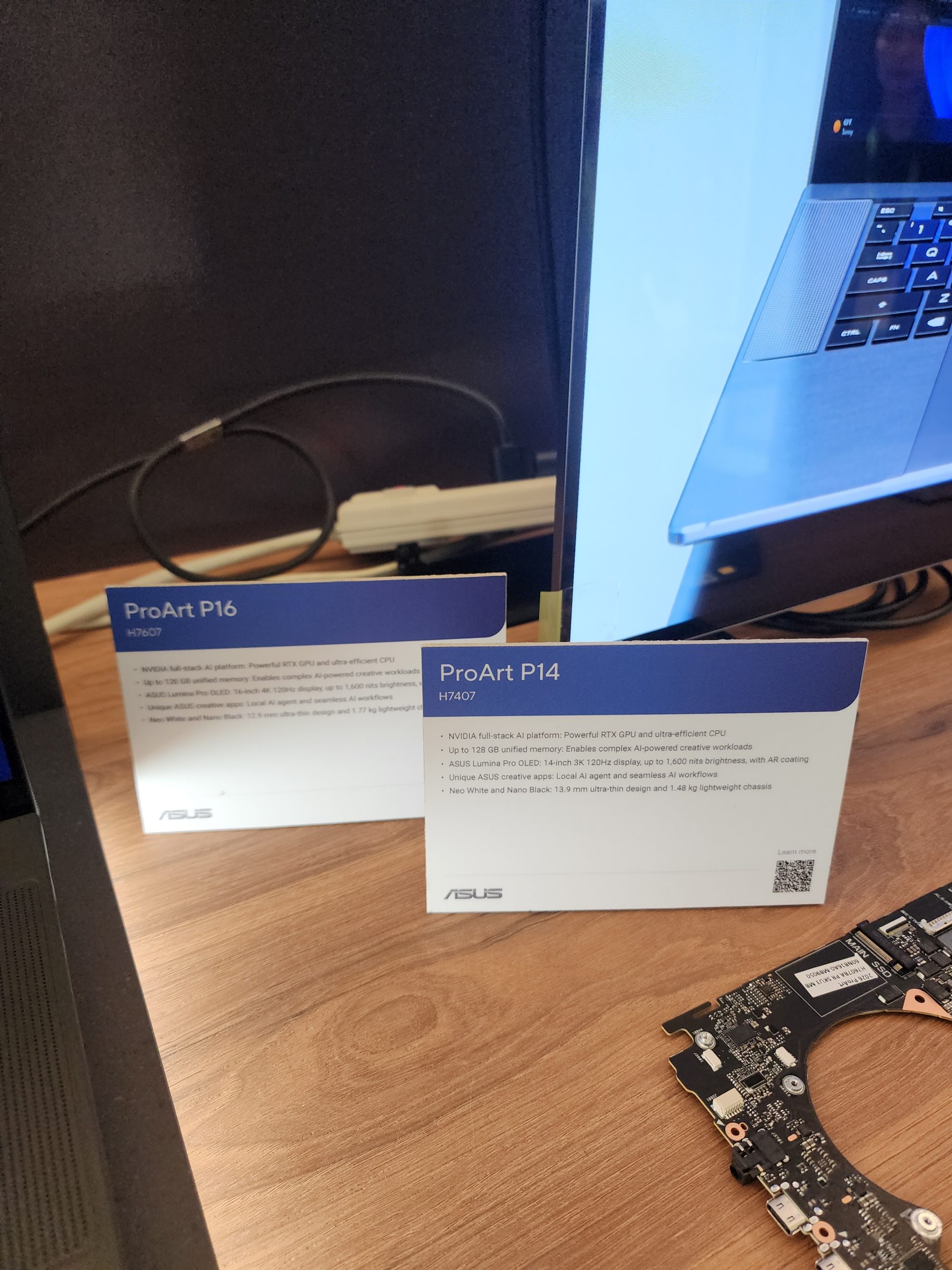 Two ASUS information cards titled 'ProArt P16' and 'ProArt P14' display specifications on a wooden table beside a computer motherboard.