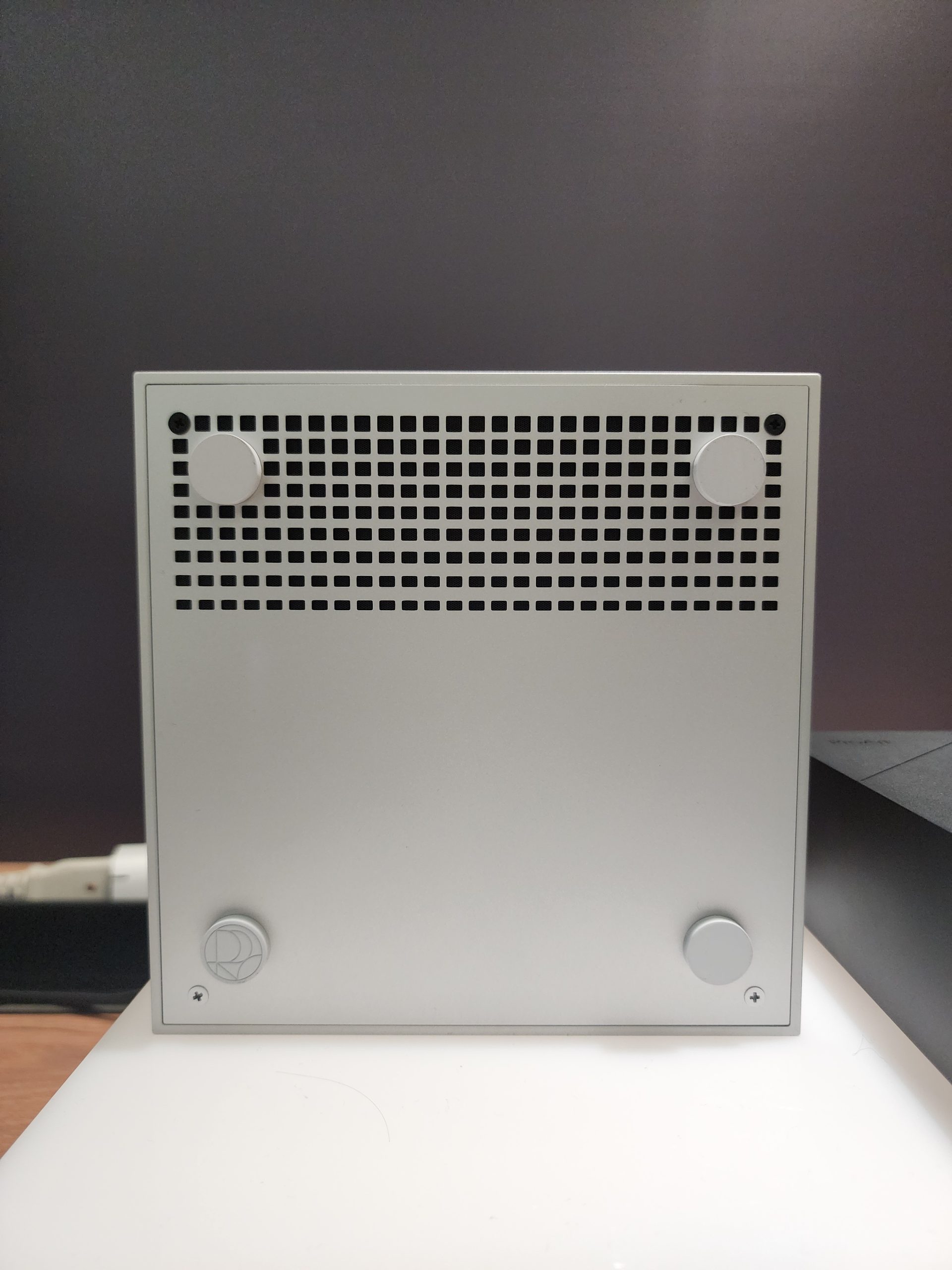 A silver Raidho Acoustics TD1.2 speaker with a grid-patterned front panel standing on a white surface.