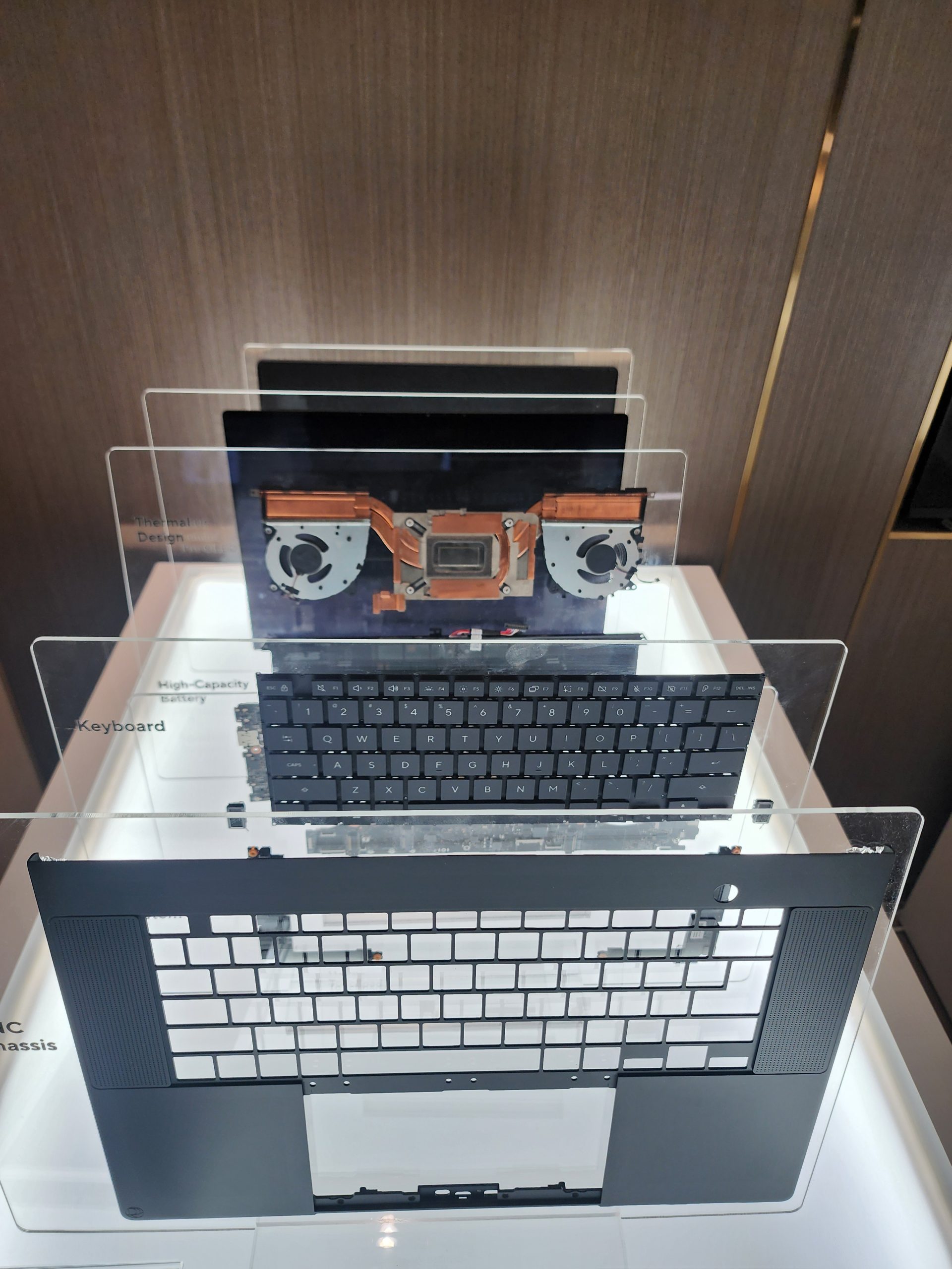 A laptop's internal components are displayed, including a thermal module, keyboard labeled 'High-Capacity Battery,' and outer chassis on transparent layers.