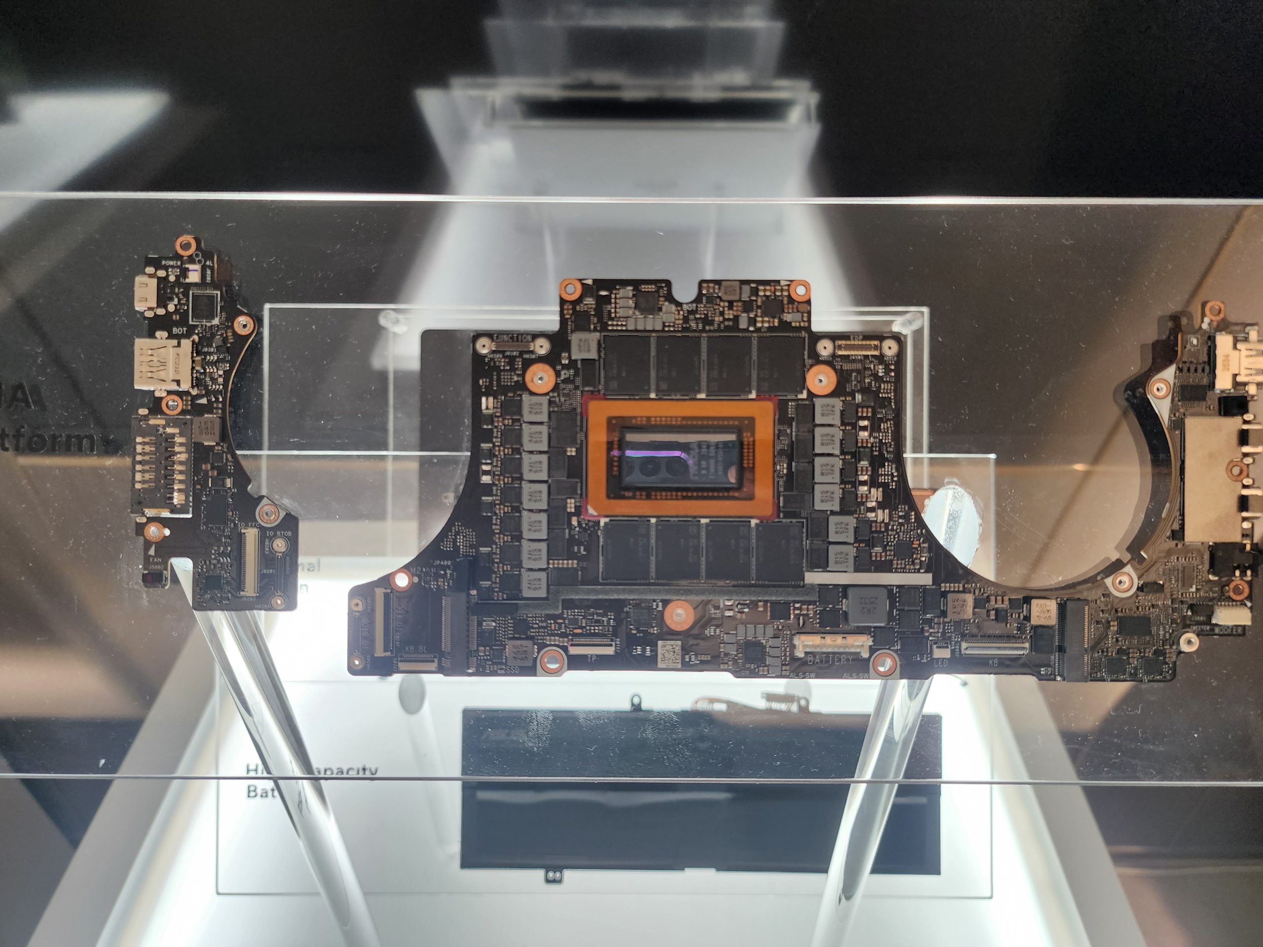 A disassembled motherboard with visible circuit components is displayed under glass at an exhibition.