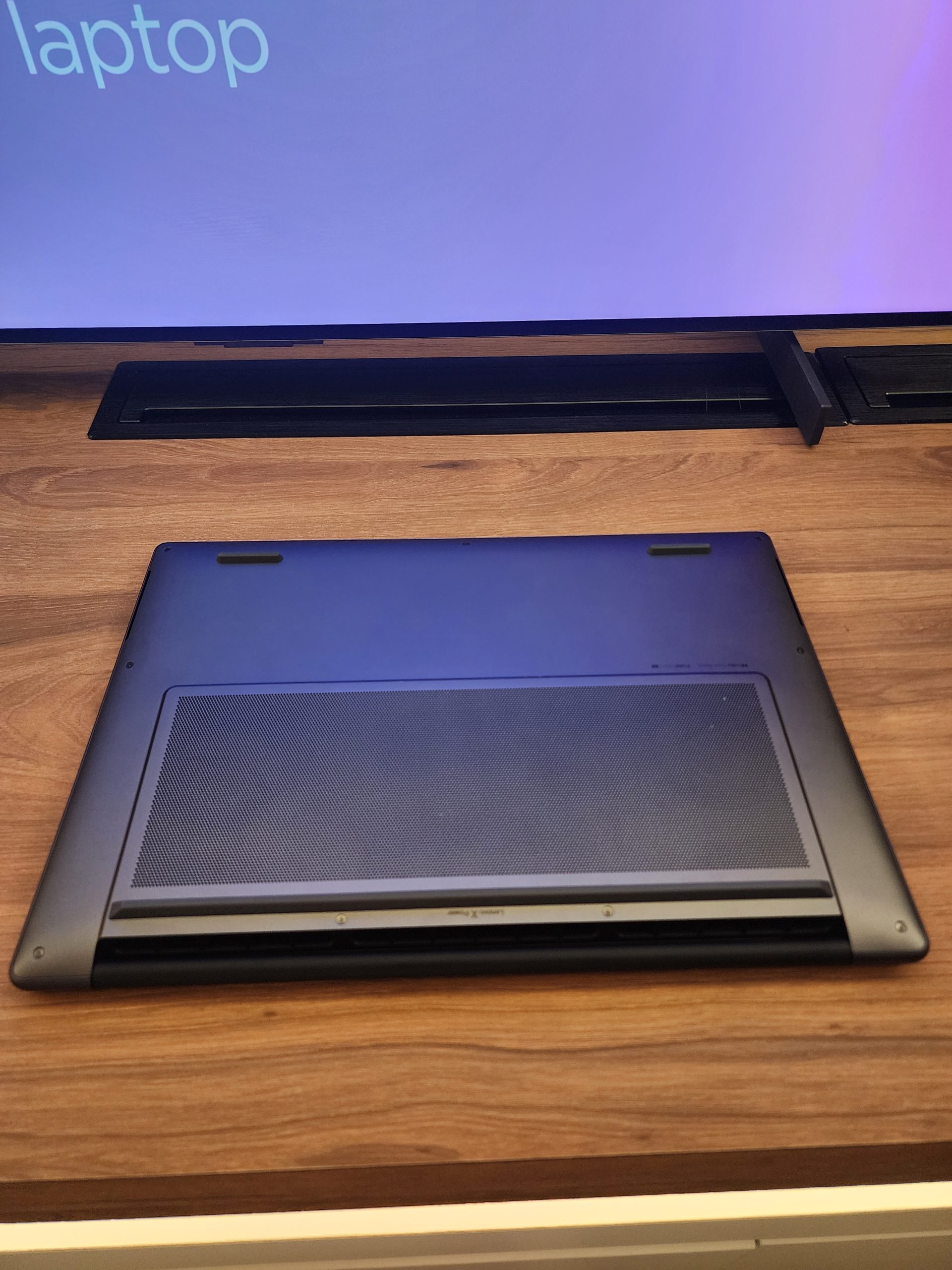 A closed laptop viewed from the bottom, showing its ventilation panel and sleek design, with part of the screen displaying the partially visible text 'laptop'.