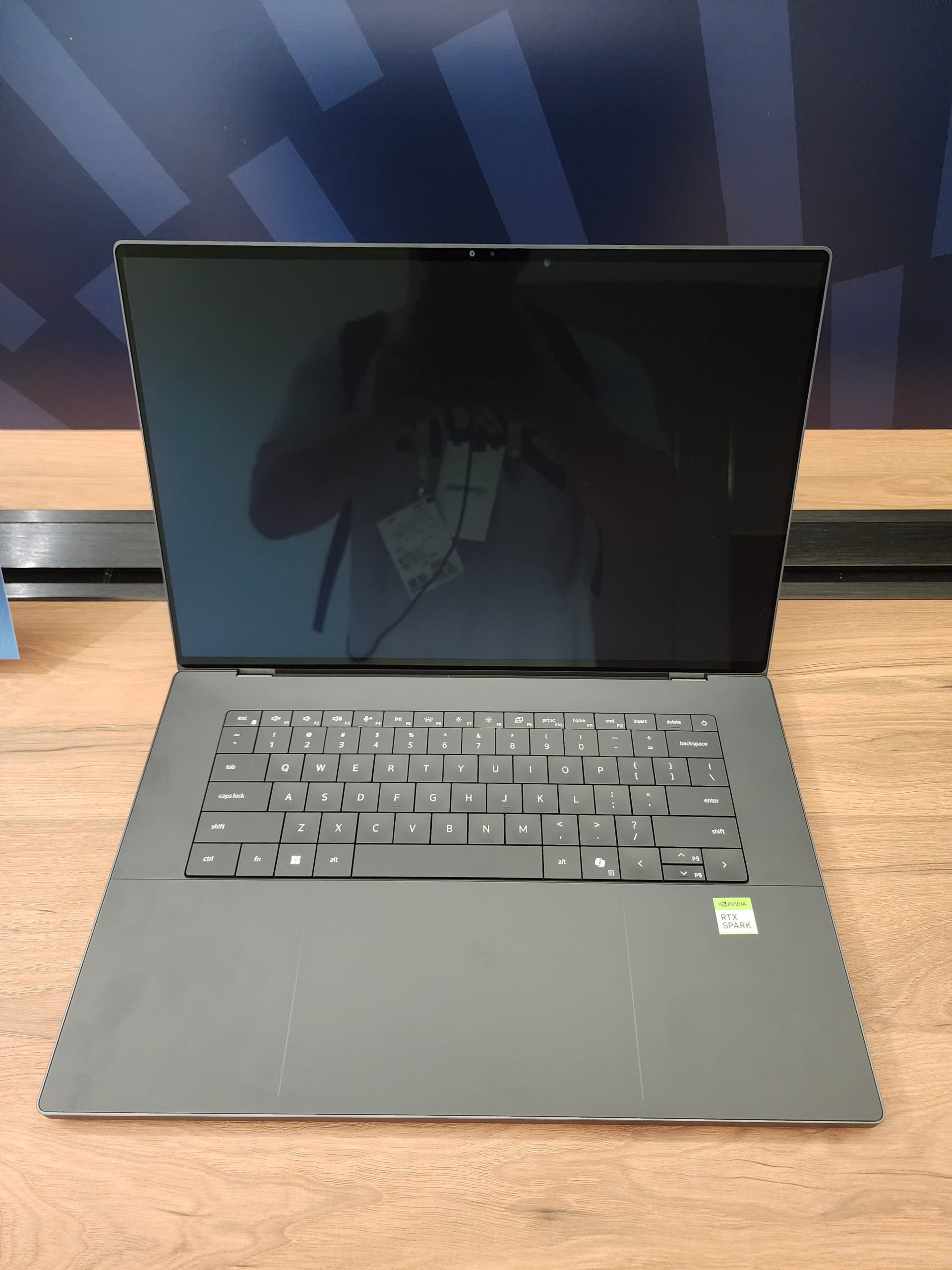 A laptop with a visible 'NVIDIA RTX 50AK' sticker on the palm rest is open on a wooden table.