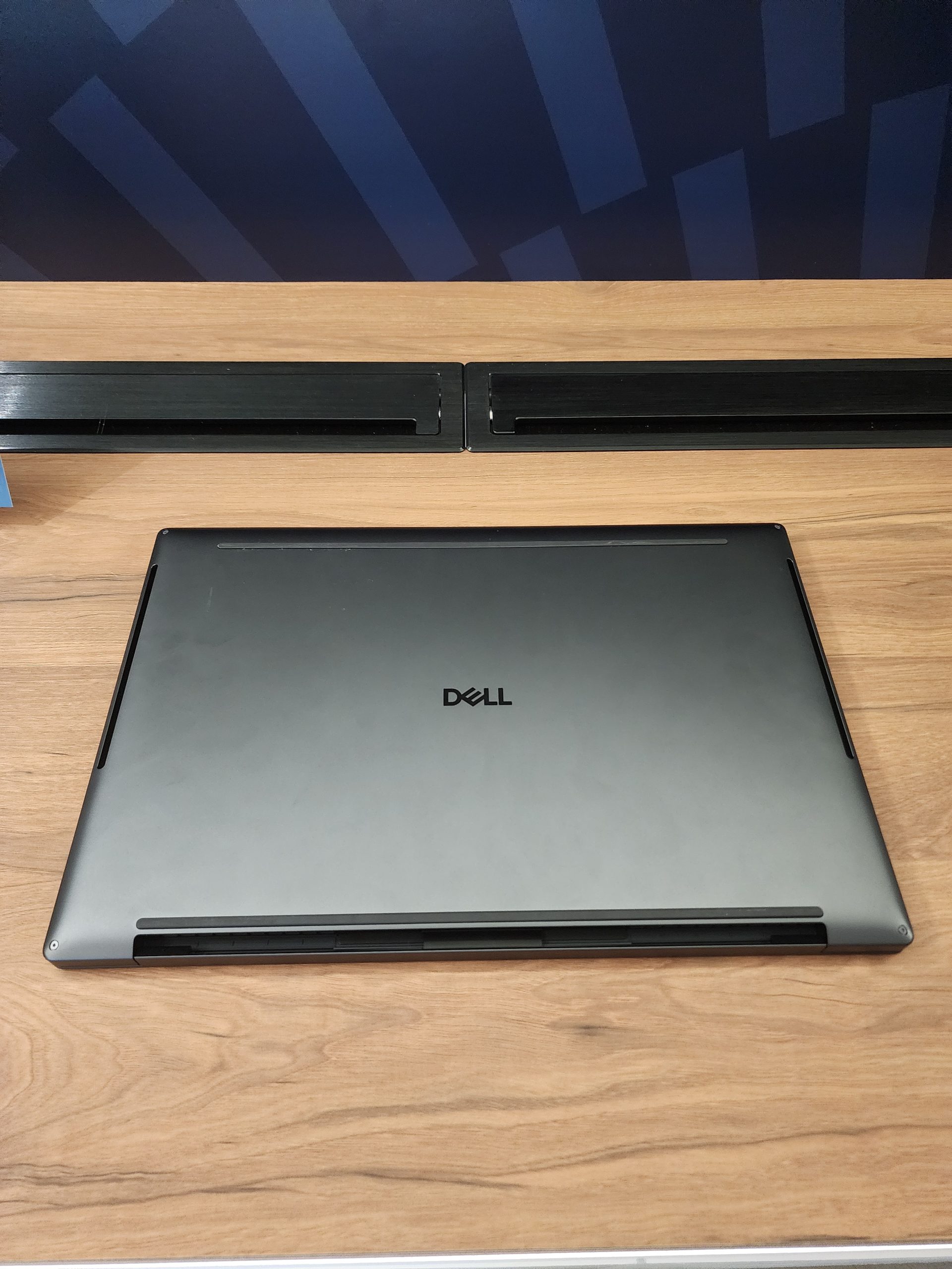 A closed Dell laptop on a wooden desk with a dark blue geometric pattern backdrop.