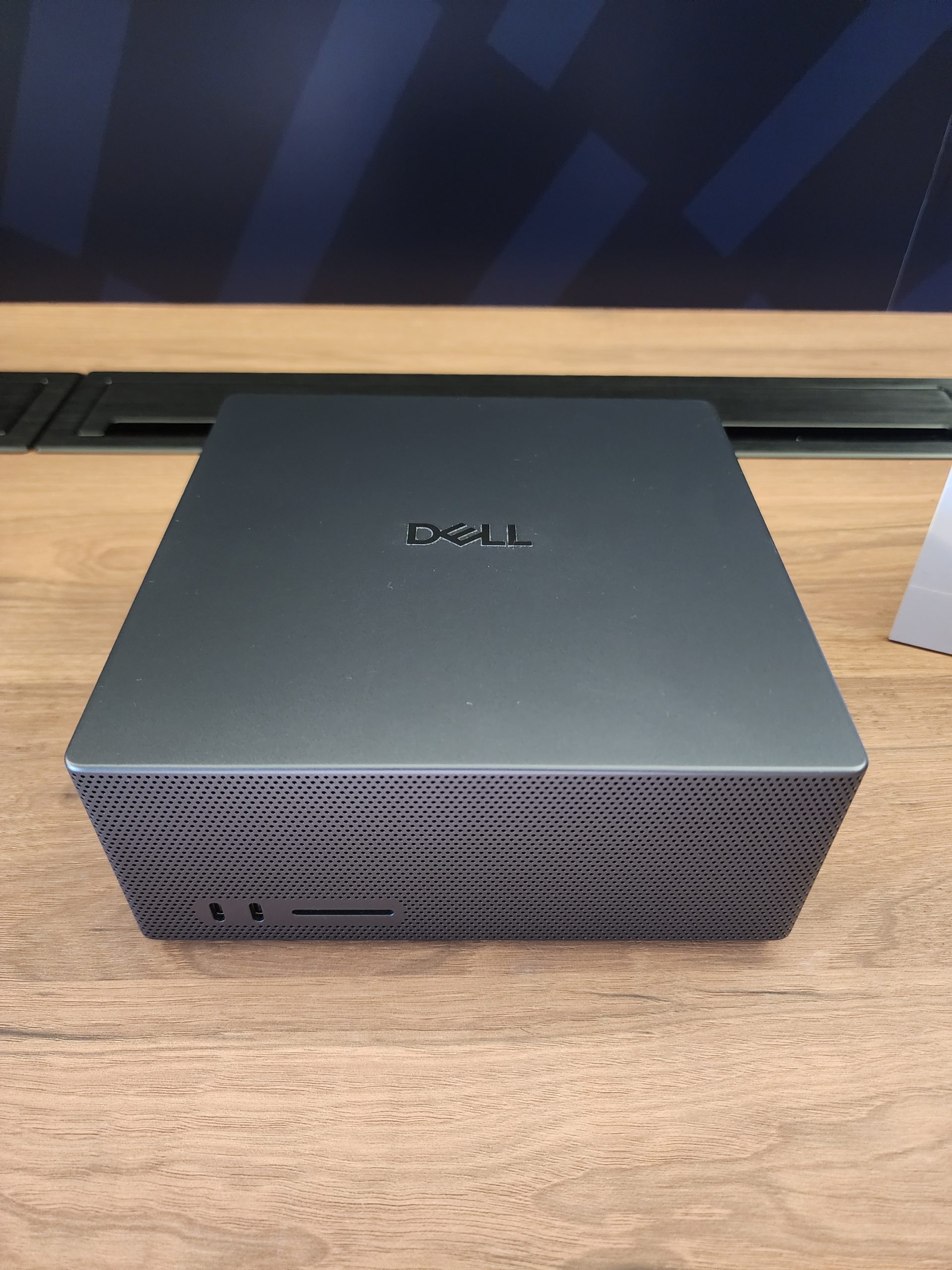 A Dell mini PC in a compact black casing is placed on a wooden surface.