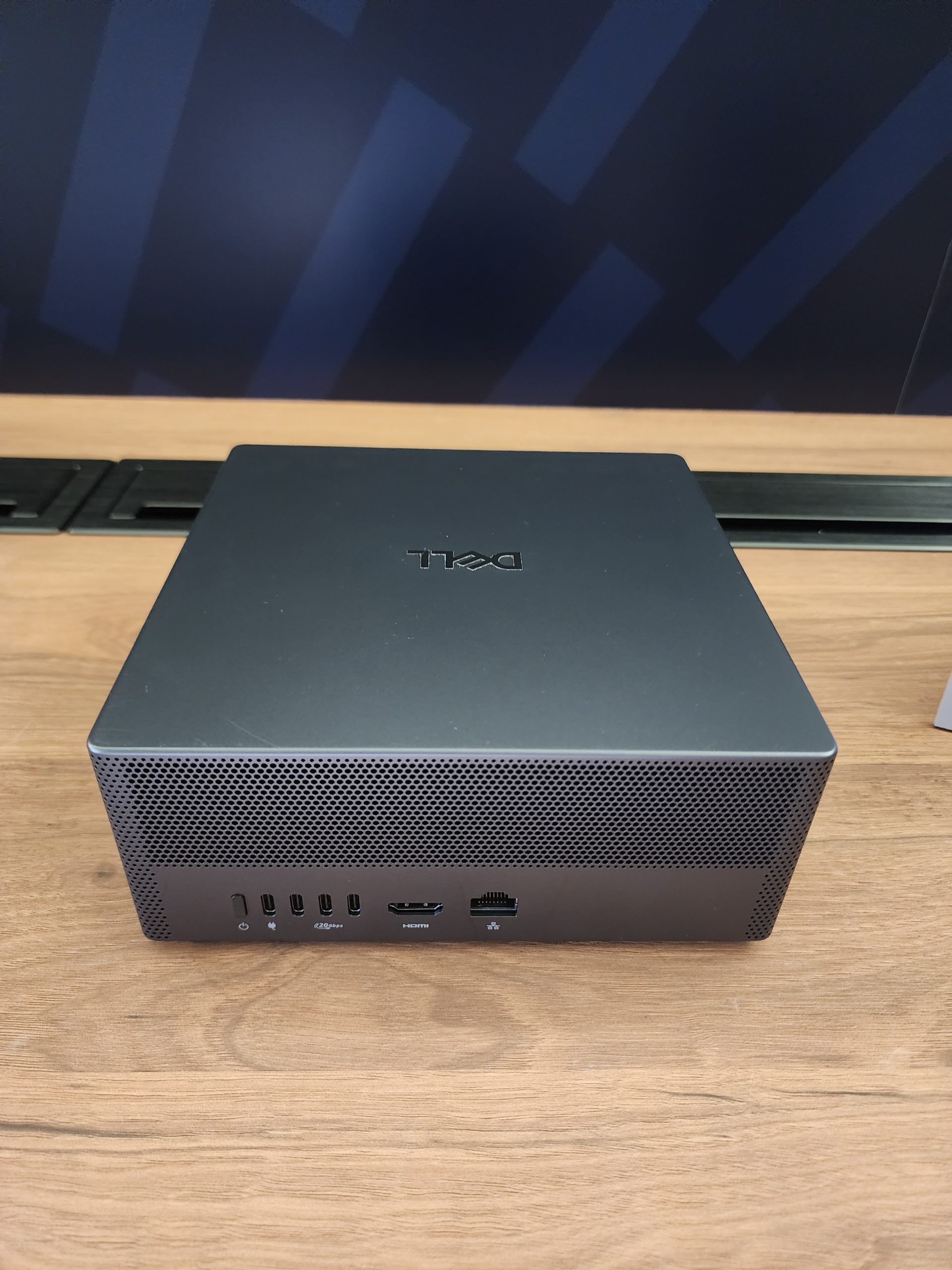 A Dell mini PC with multiple ports, including USB-C, HDMI, and Ethernet, is shown on a wooden surface.