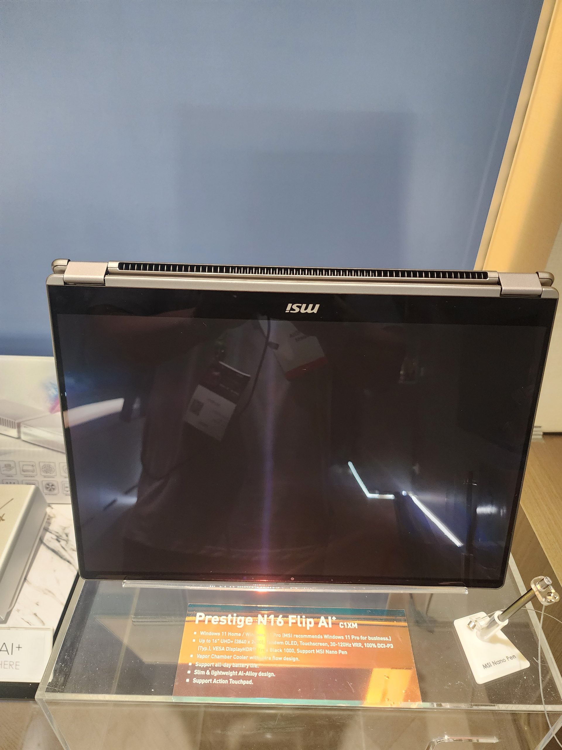An MSI laptop labeled 'Prestige N16 Flip A1' is displayed on a stand, with a sign mentioning its features such as a 14 UHD display, touch screen, and support for the MSI Nano Pen.