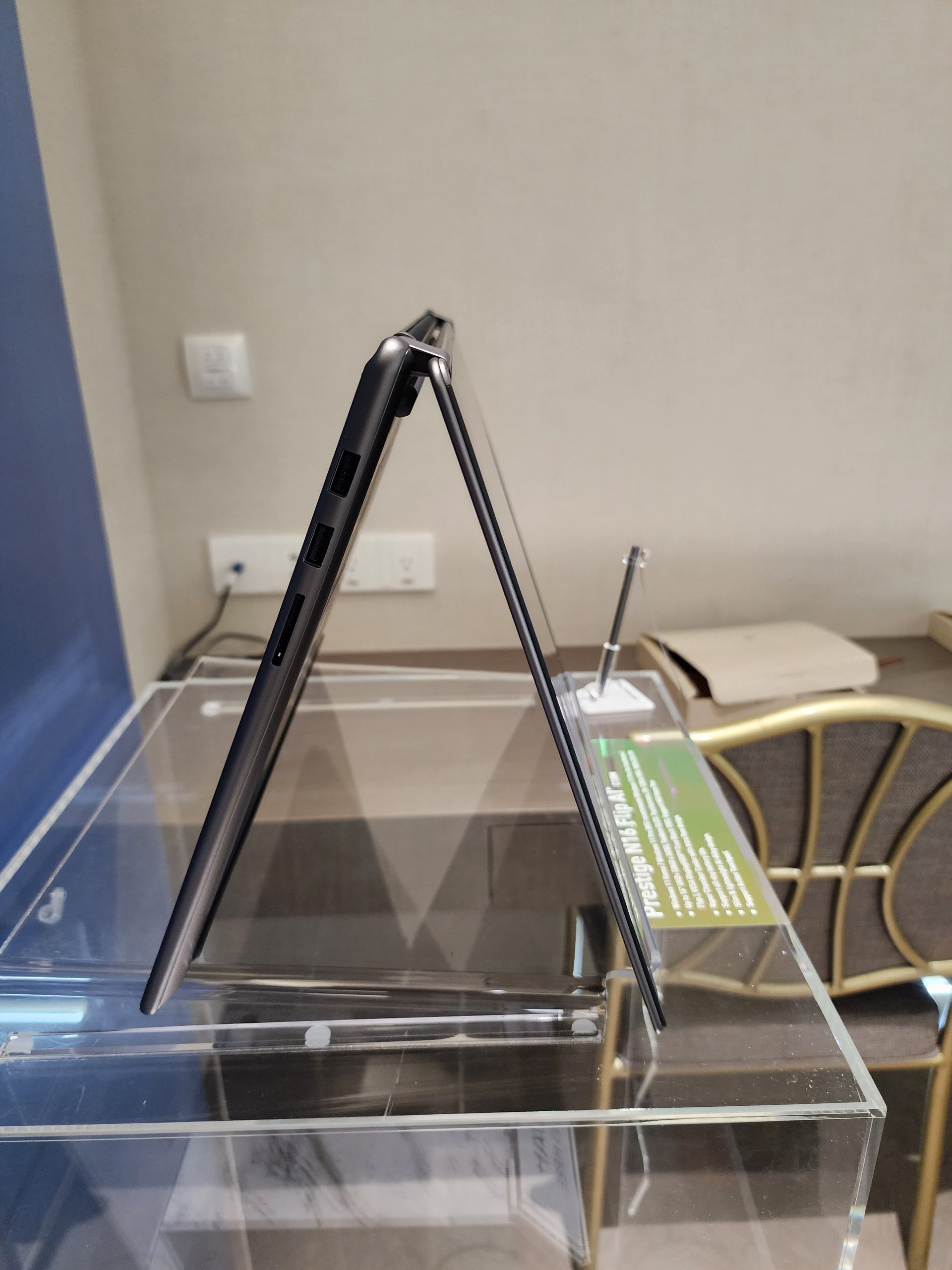A side view of an MSI Prestige 16 Flip AI laptop displayed on a clear stand in a triangular, tent-like position.