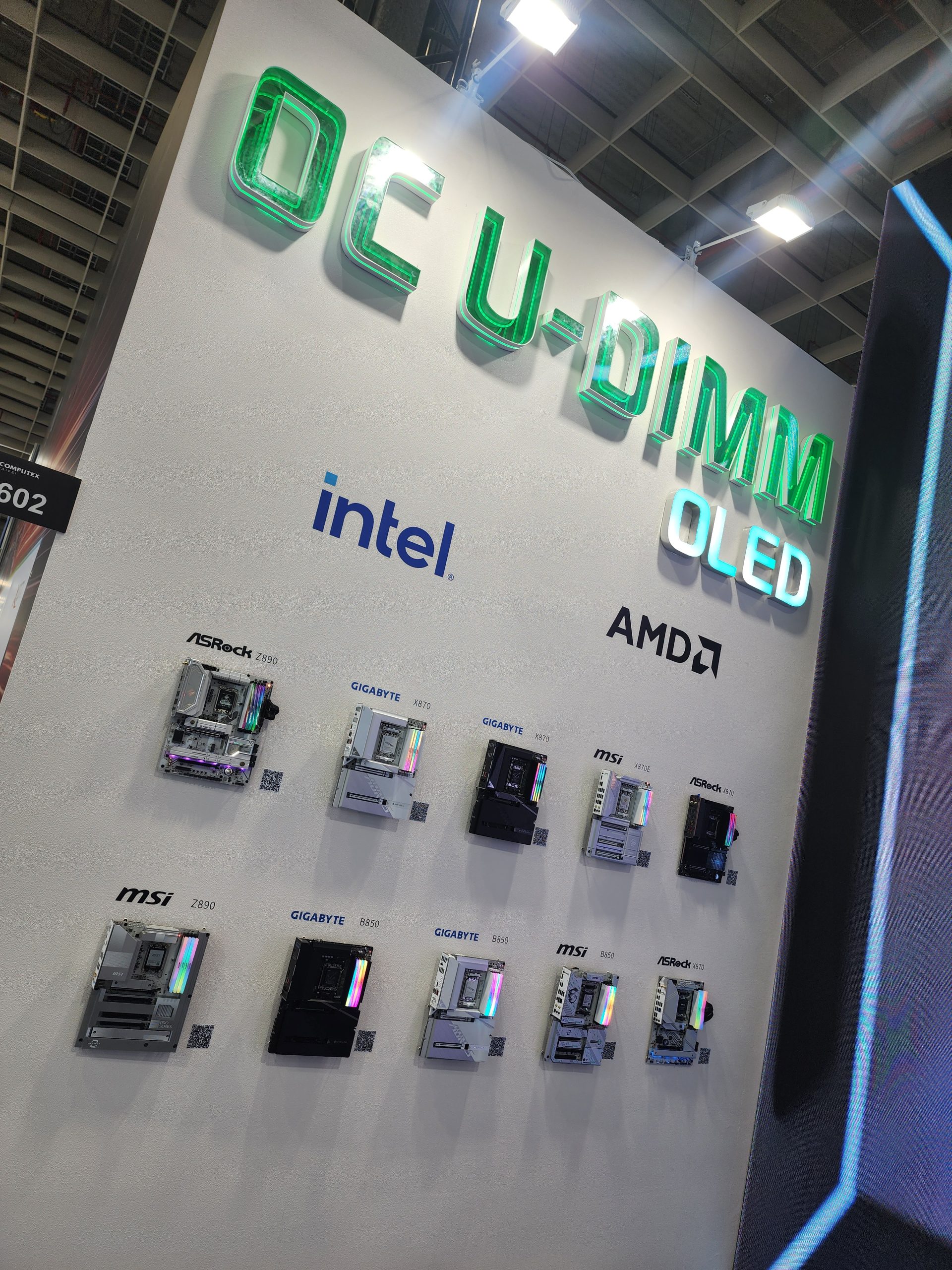 A display wall at Computex showcases various motherboards, including ASRock Z690, GIGABYTE X670, MSI X670E, GIGABYTE B650, and MSI B650E, under a sign reading 'OCU-DIMM OLED,' with both Intel and AMD logos visible.