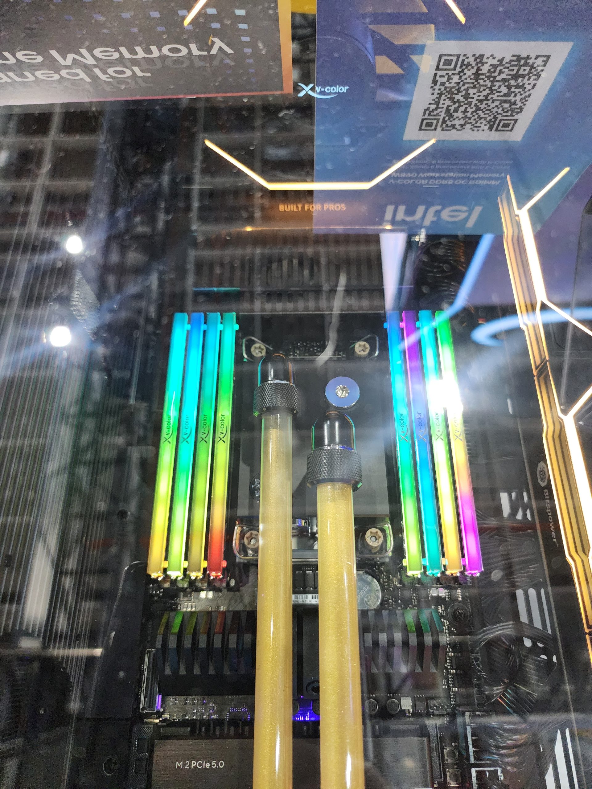 A computer motherboard featuring XPG RGB RAM sticks and a label indicating 'M.2 PCIe 5.0' under a glass surface.