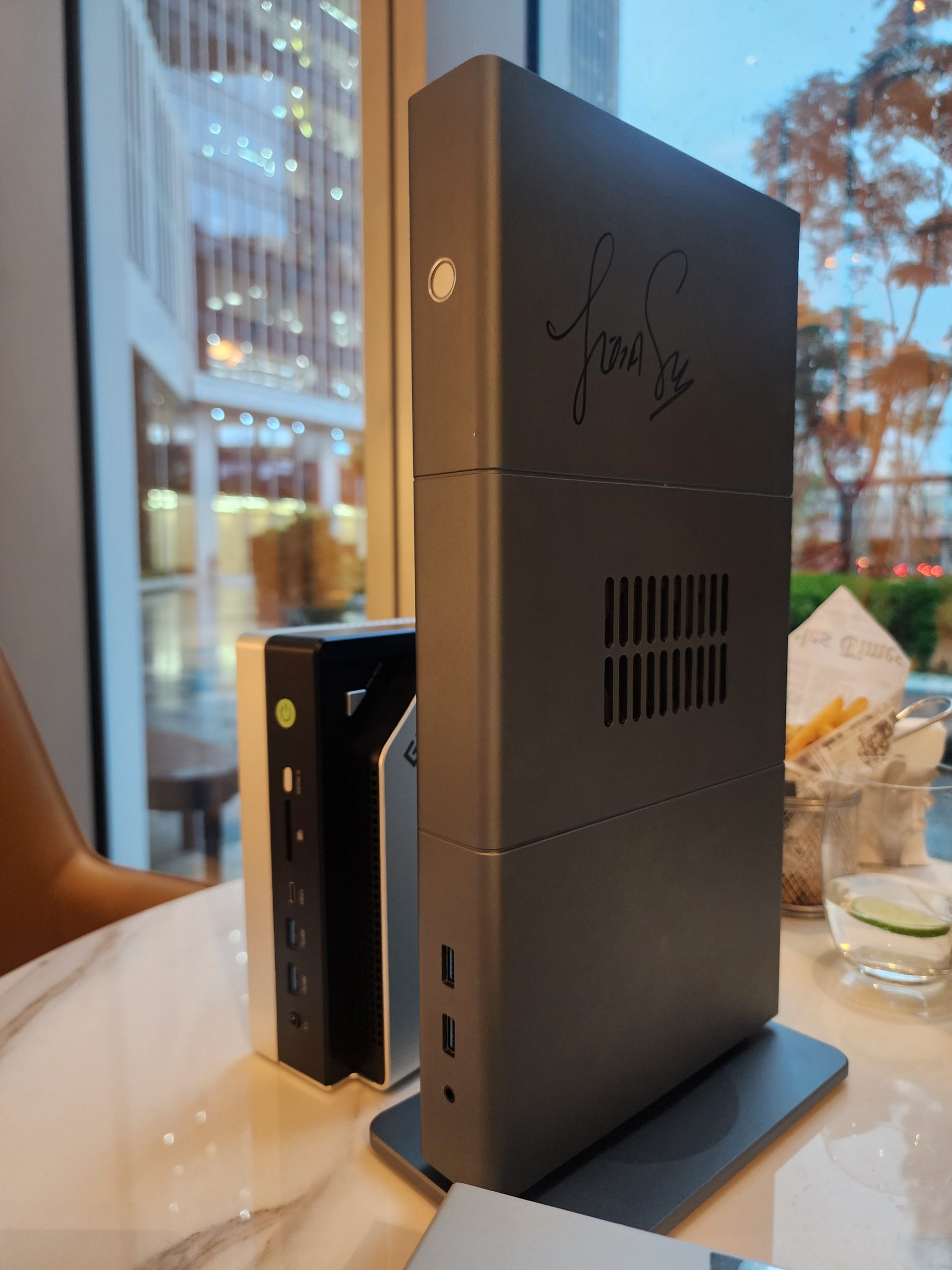 Three compact desktop computers are lined up on a marble table with the tallest unit signed by an unknown person and two other smaller units featuring USB ports on the front panel.