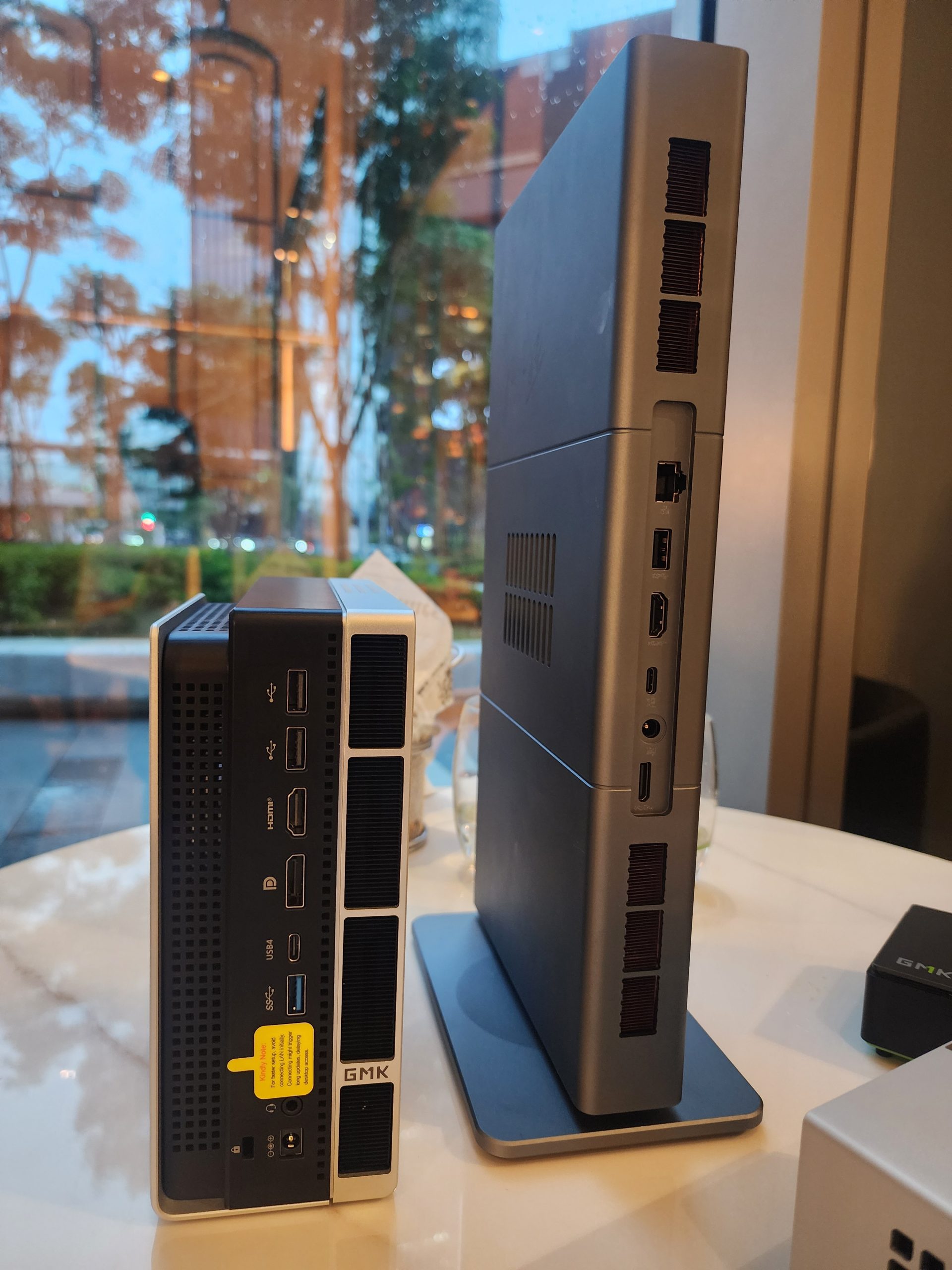 A GMK NucBox 7 mini PC is shown side by side with a slim, unbranded desktop PC, highlighting their compact designs and various port options.