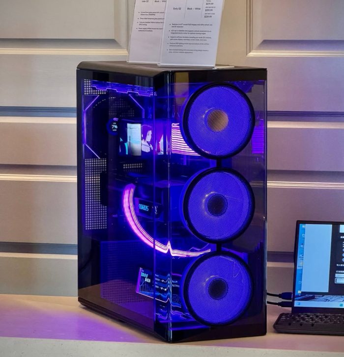 A custom-built gaming PC with vibrant purple lighting and prominent front fans, connected to a laptop with visible on-screen text.