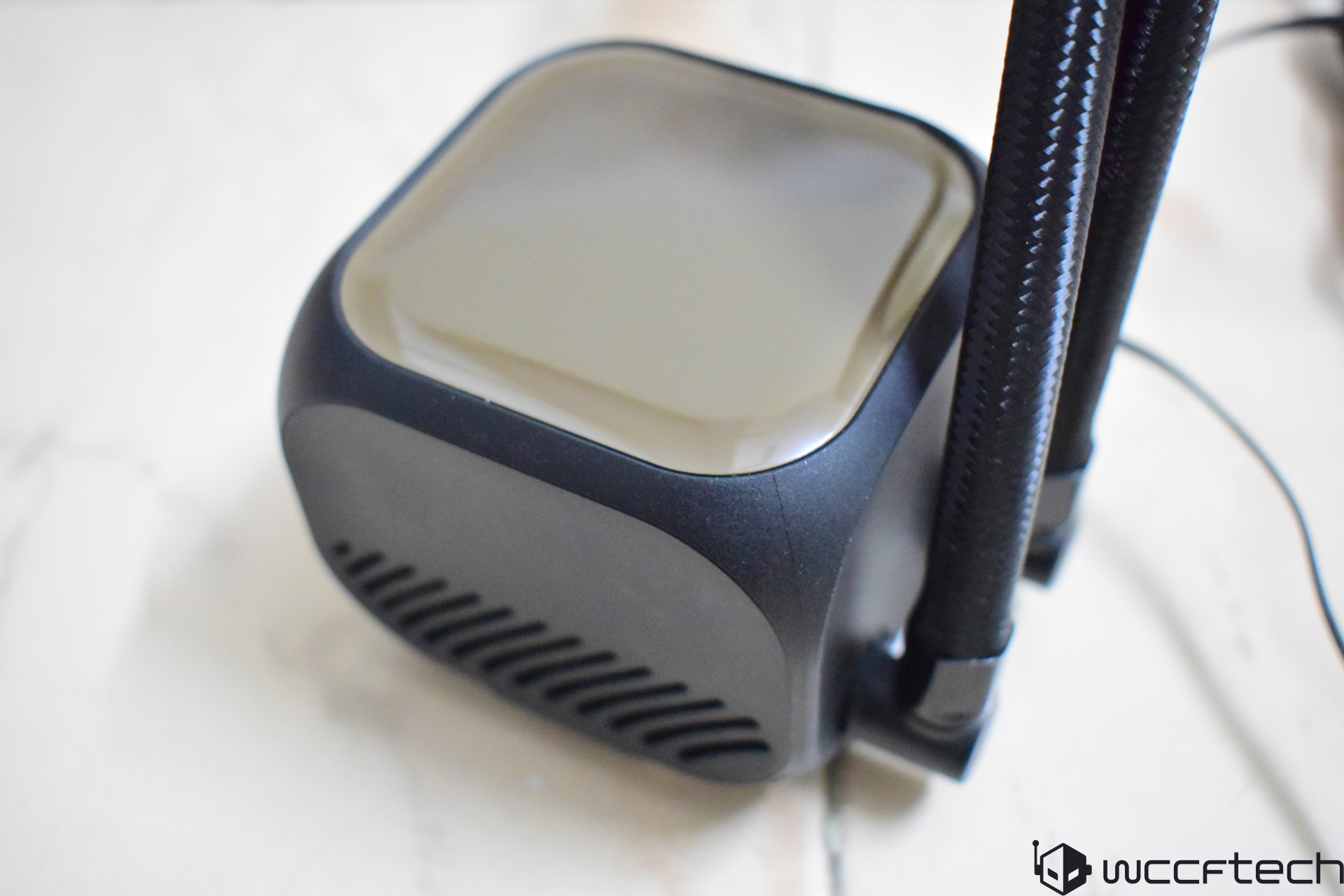 A close-up of a black and gray unbranded CPU liquid cooler with braided tubes on a light surface.