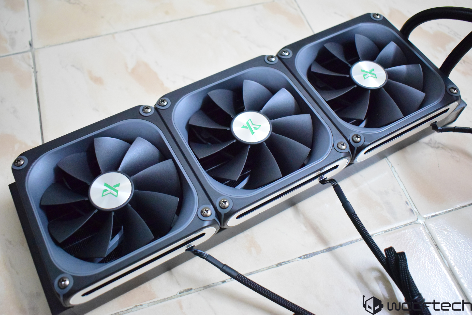 Three black and silver fans with a green X logo, part of a computer cooling system, are shown from the top view.