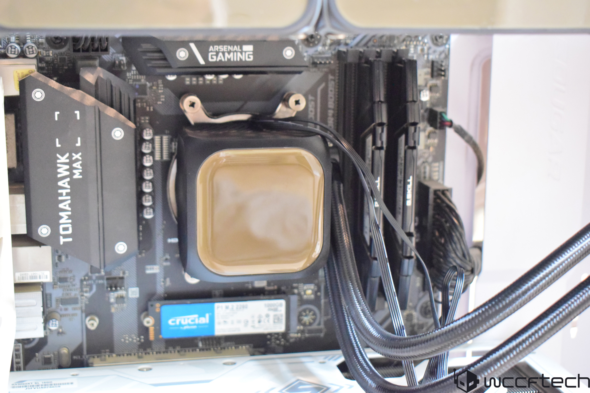 An MSI Tomahawk Max motherboard with an 'Arsenal Gaming' logo, featuring a Crucial P1 M.2 SSD and cooling tubes connected to a CPU cooler.