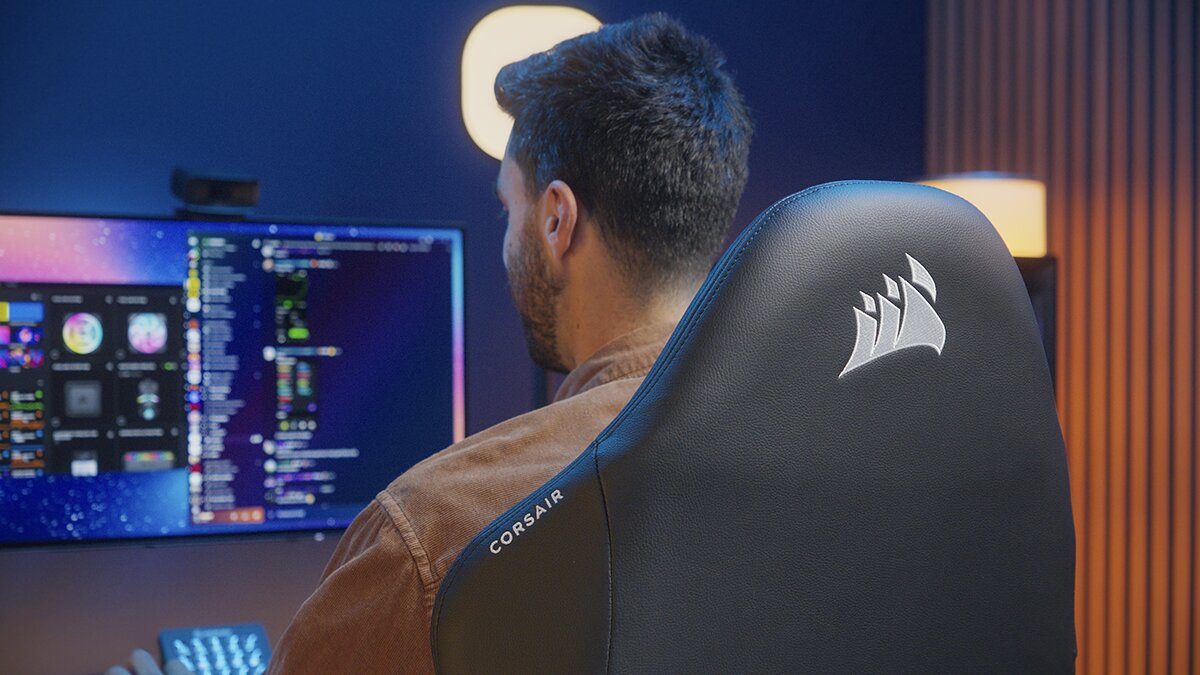 A person sits at a desk using a computer, with the back of their Corsair gaming chair visible in the foreground.