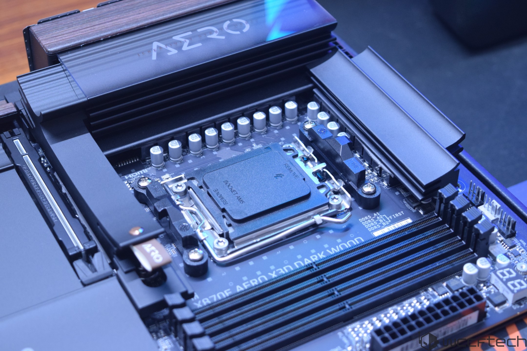 A GIGABYTE X670E AERO X3D DARK WOOD motherboard with visible DIMM slots and a socket labeled 'REMOVE'.