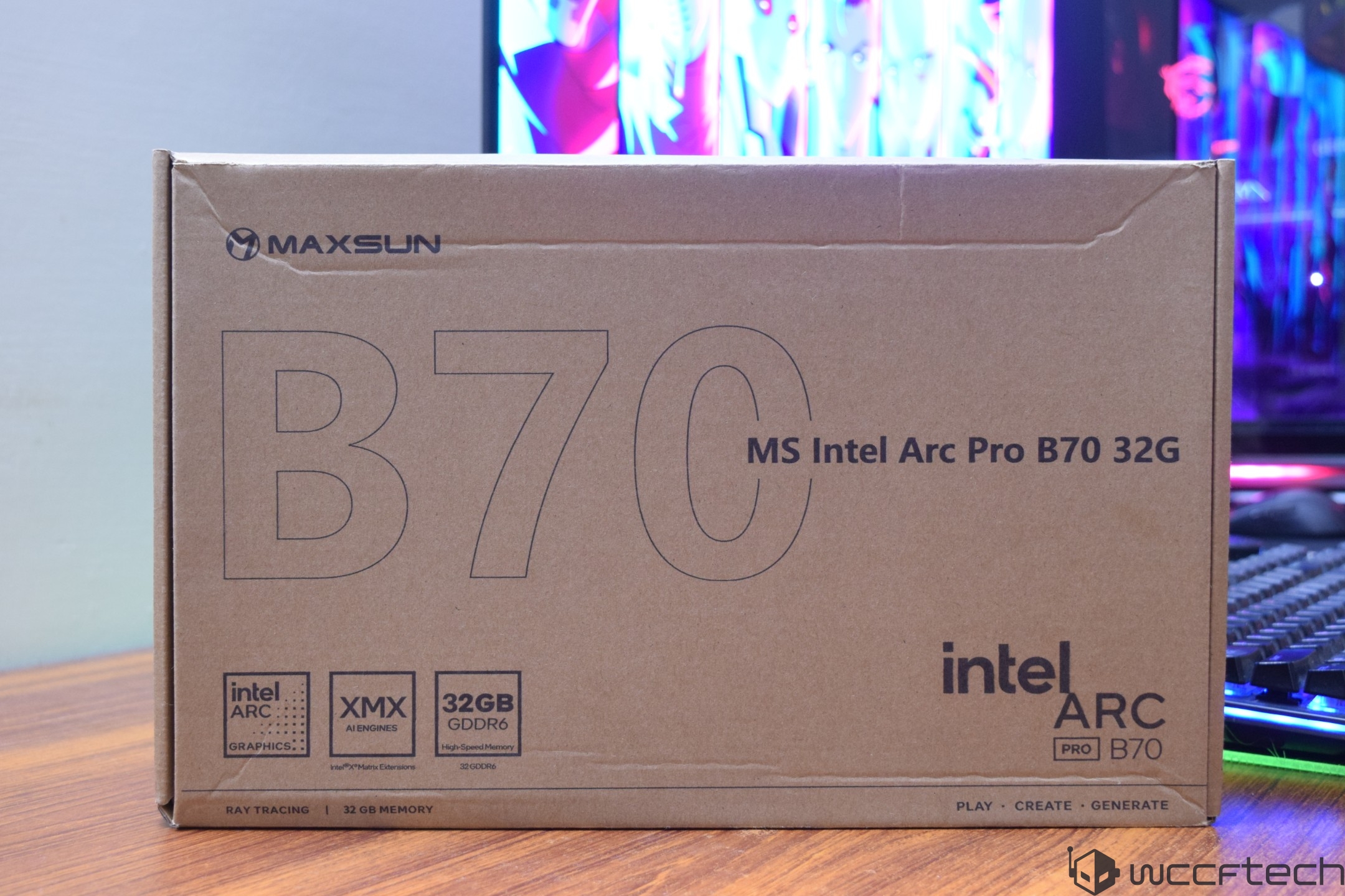 A Maxsun box for the Intel Arc Pro B70 32G graphics card is shown on a wooden surface with colorful computer components in the background.