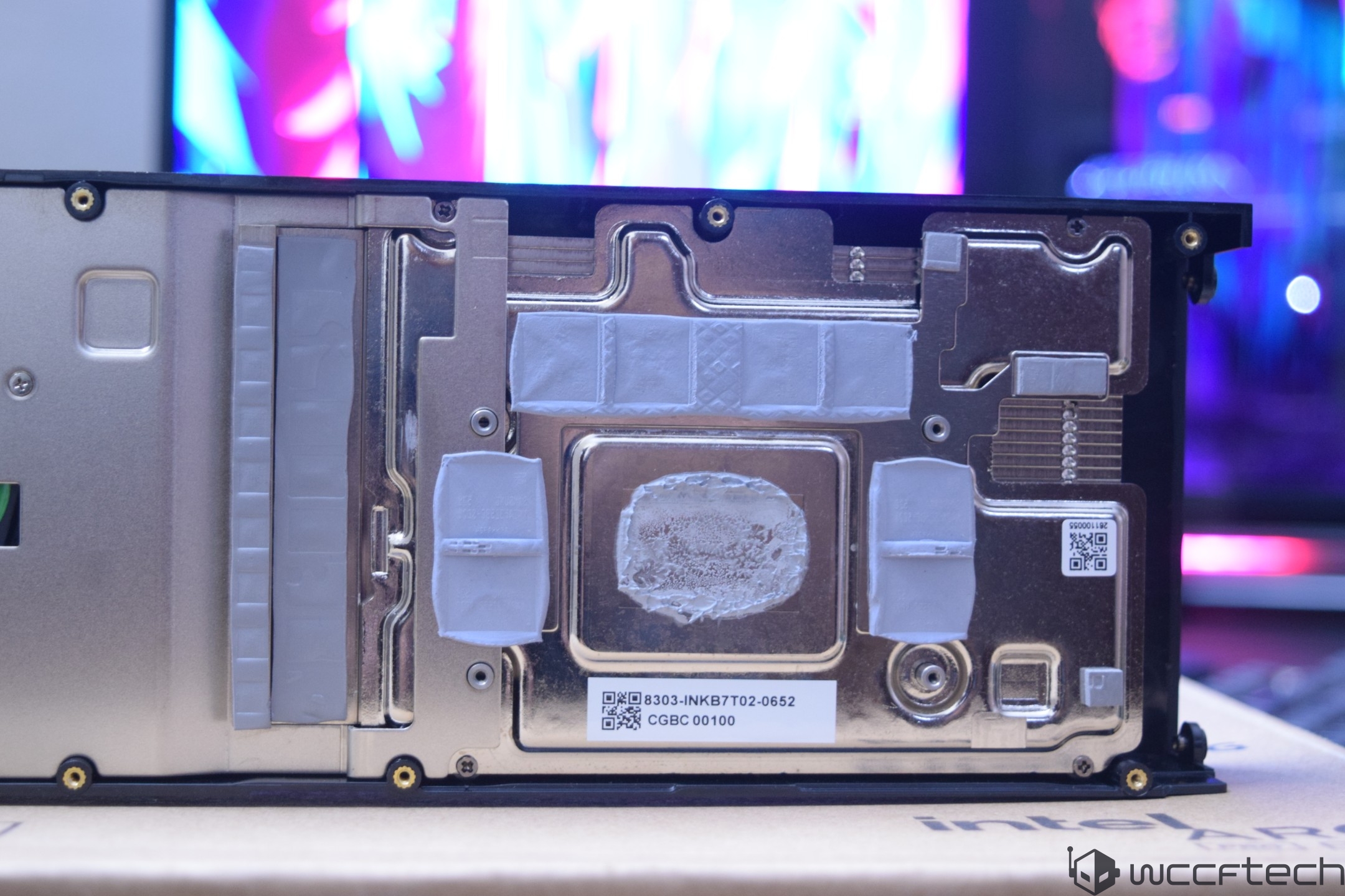 Close-up of the backplate of a graphics card with visible thermal paste and QR codes, placed on a box with partial 'Intel' branding.