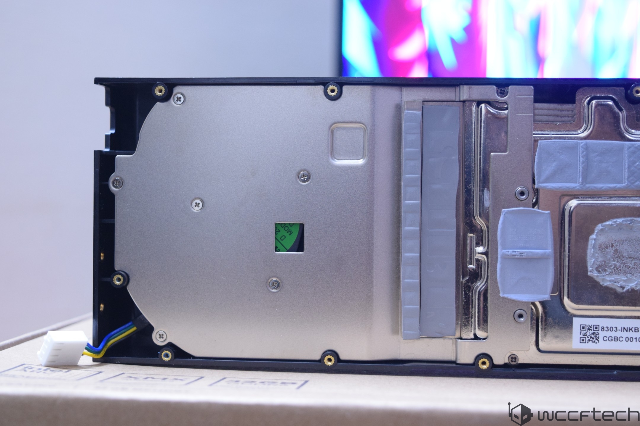 The rear view of a partially disassembled NVIDIA graphics card shows the metal backplate and thermal padding, placed on top of a cardboard box.