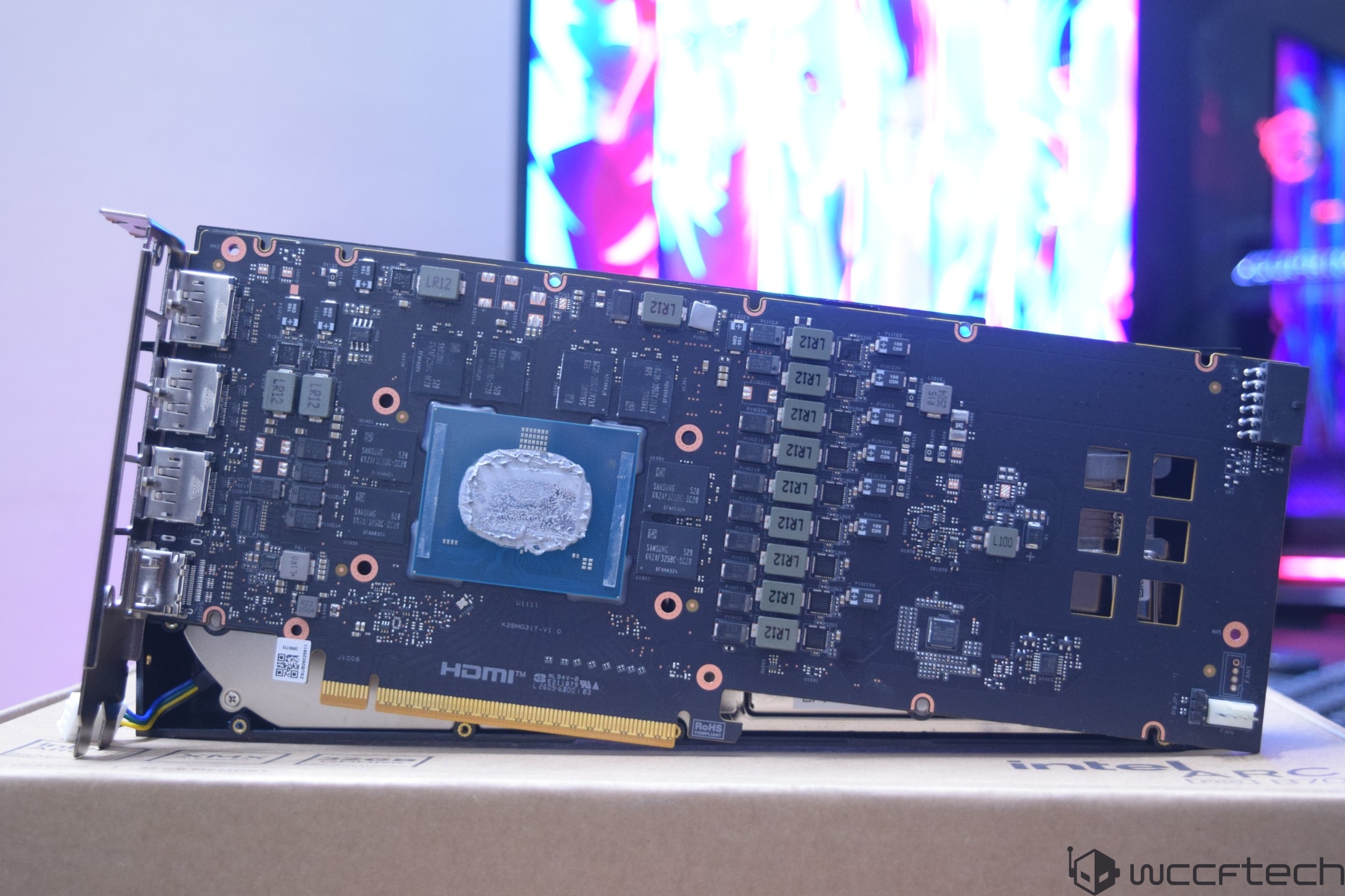 A graphics card with visible HDMI ports and exposed components is placed on an Intel Arc-branded box, showing thermal paste applied on the chip.