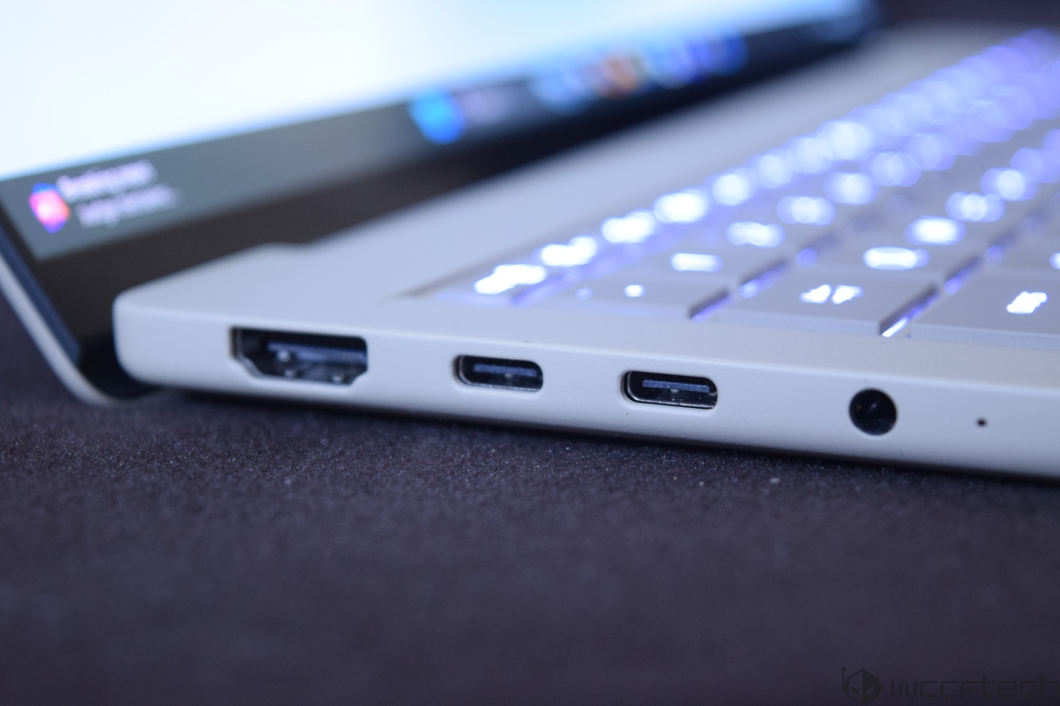 A close-up of an unbranded laptop's side ports, including an HDMI port, two USB-C ports, and a headphone jack, with a partially visible illuminated keyboard.