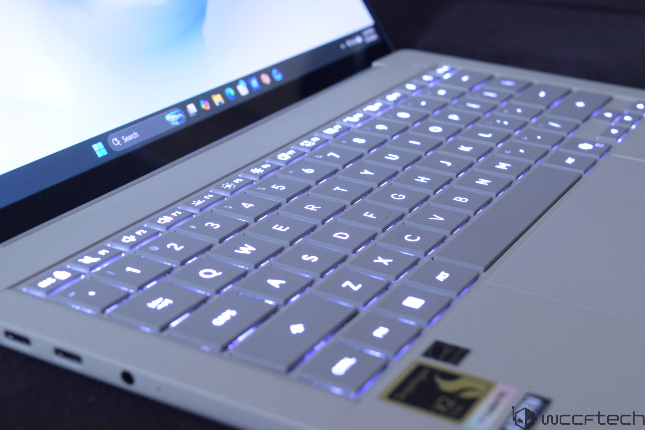 An unbranded laptop with a glowing keyboard and visible Windows search bar on the screen.