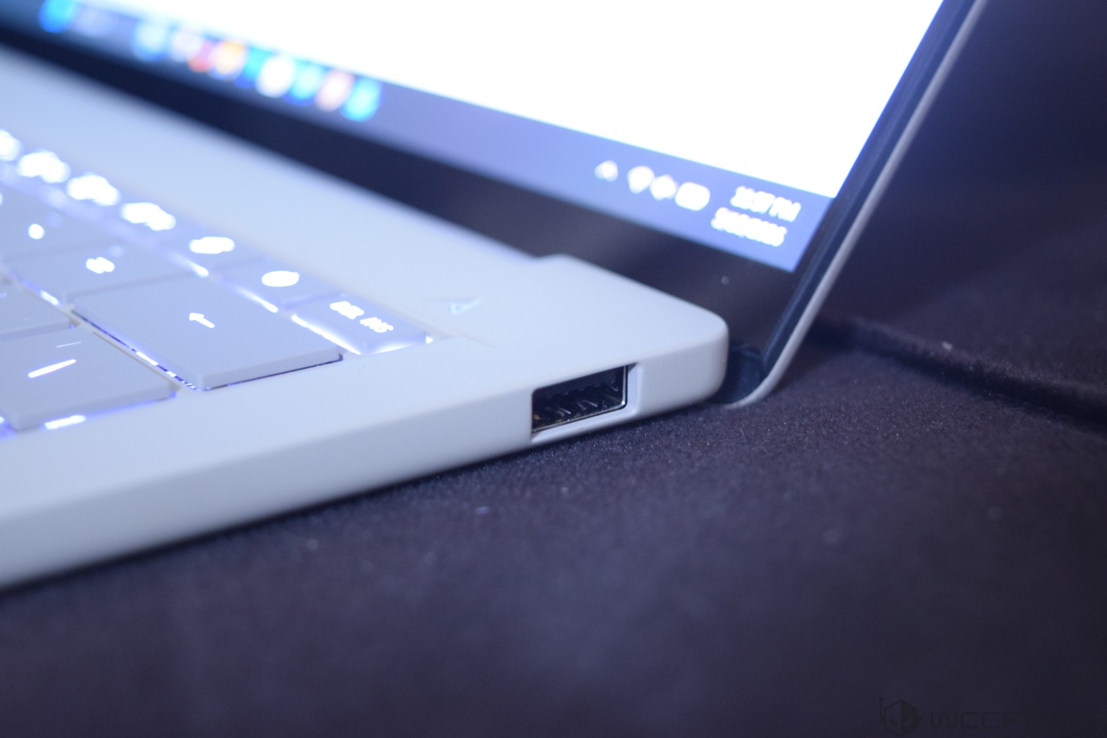 A close-up of an unbranded laptop showing USB port and illuminated keyboard keys, with a portion of the screen displaying '5:07 PM' and Wi-Fi signal icons.