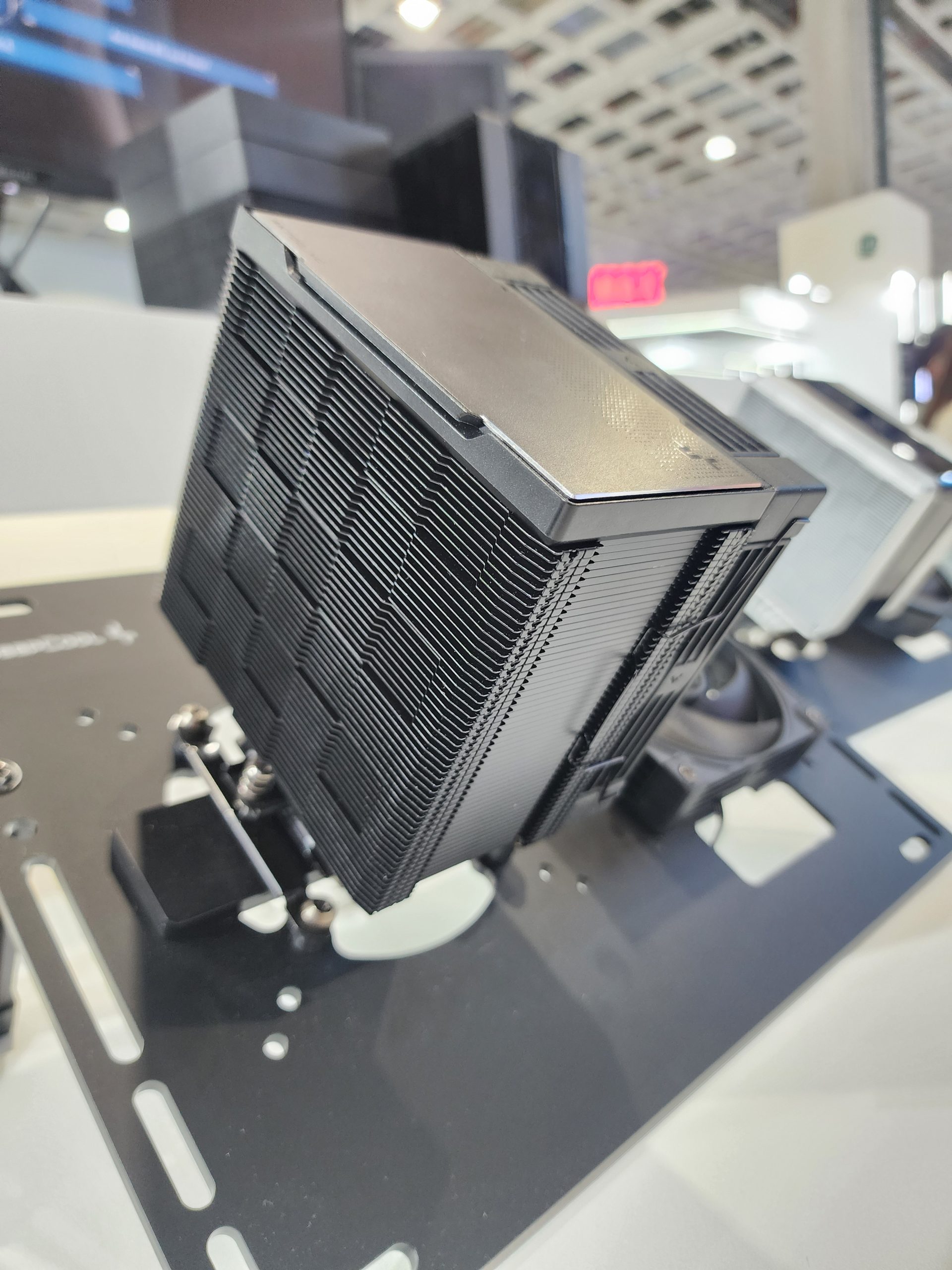 A large black CPU cooler with stacked fins is displayed on a mounting bracket at an exhibition booth.