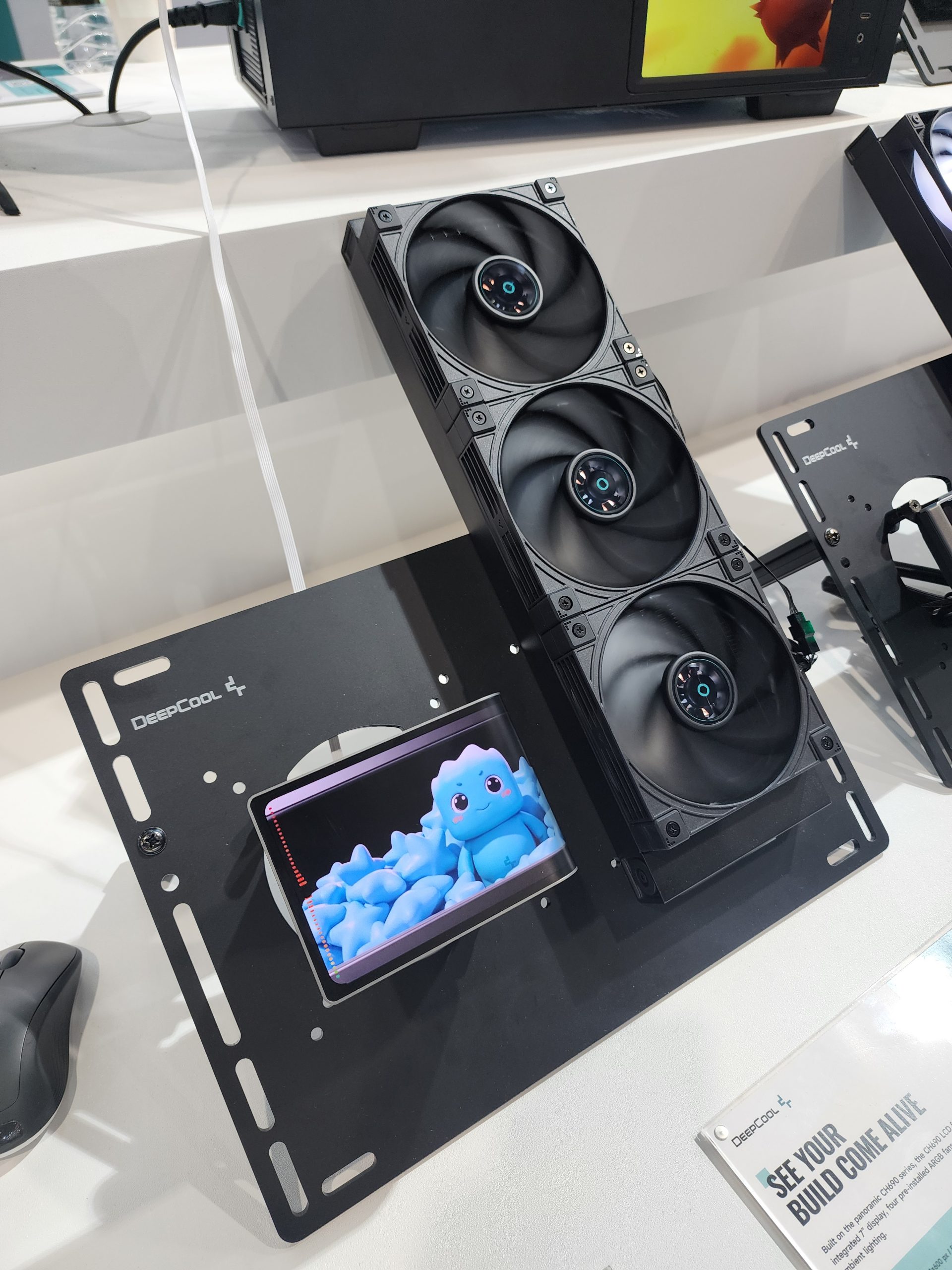 A DeepCool cooling system display featuring a triple-fan setup alongside an animated blue character on a screen with the text 'DeepCool' visible.