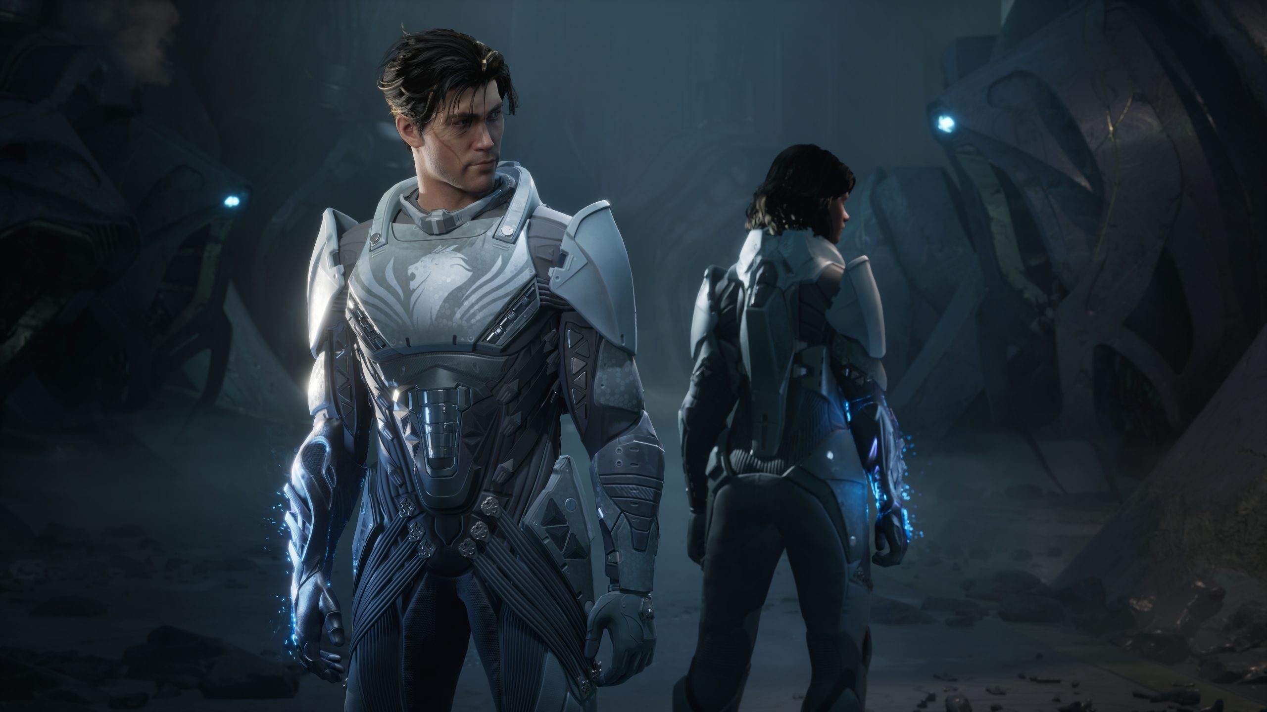 Two characters in futuristic armor stand in a dimly lit, alien environment with glowing elements, appearing to be from a video game.