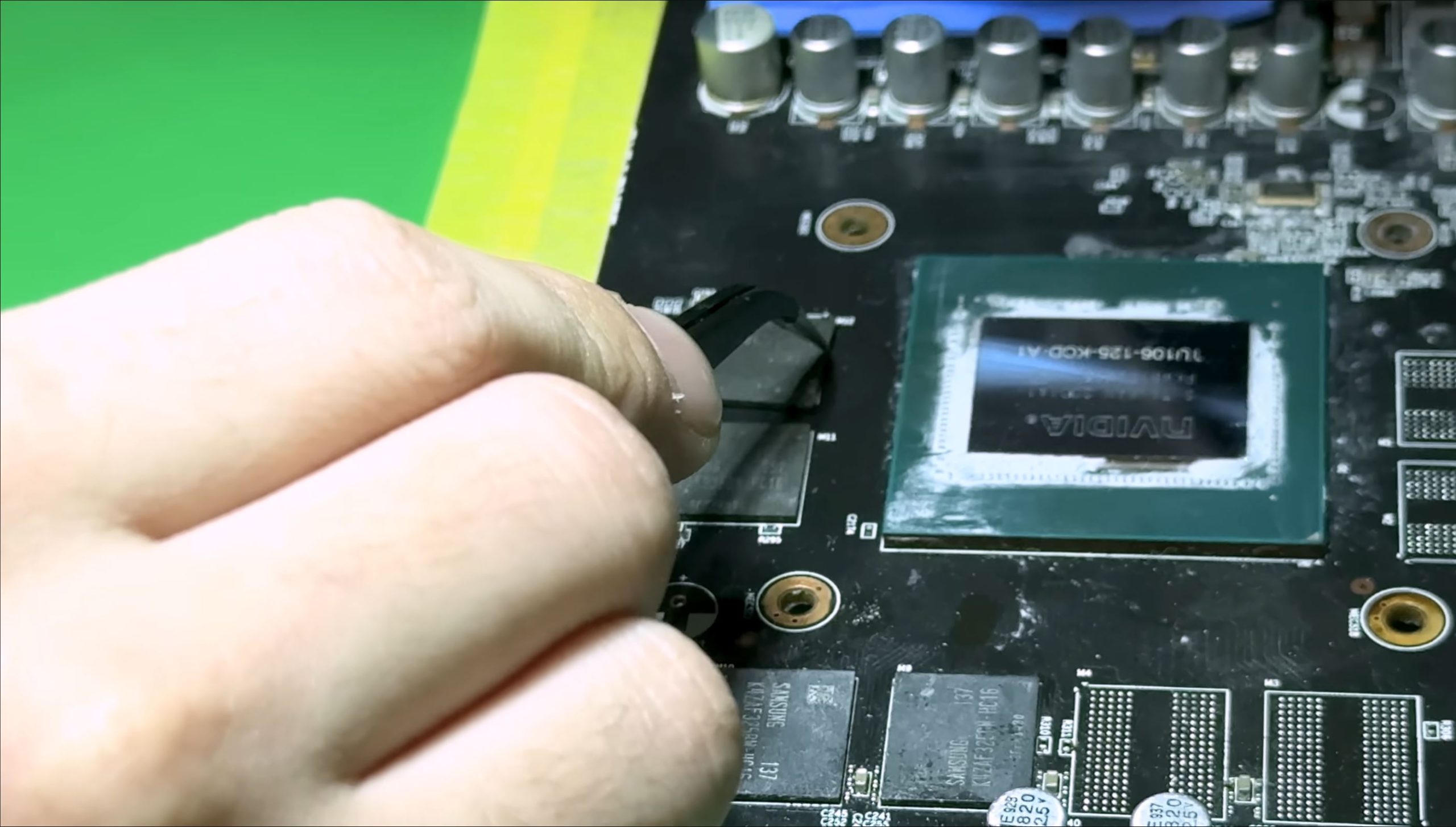 A person is using tweezers to remove or place a component near an NVIDIA graphics chip with the label '1J1165-135-K00-A1' on a circuit board.