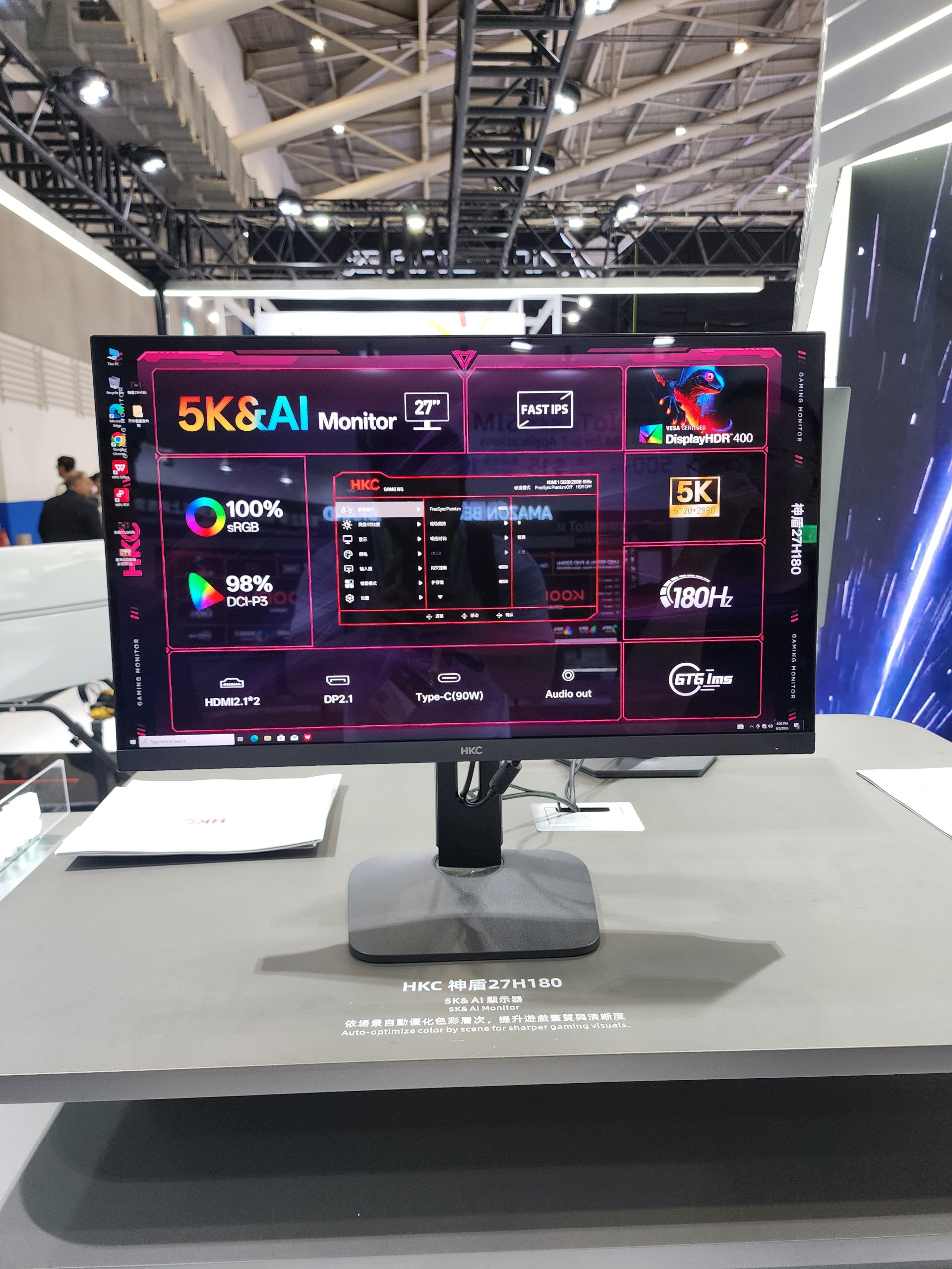 The HKC 27H180 5K monitor displays specs like '5K&AI Monitor,' 'Fast IPS,' '27 DisplayHDR 400,' and '180Hz' at an exhibition booth.