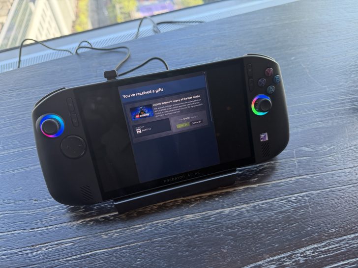 A Predator Atlas handheld gaming device is displayed on a table, showing a notification screen that reads 'You've received a gift!' with details about the game 'LEGO Batman: Legend of the Dark Knight.'