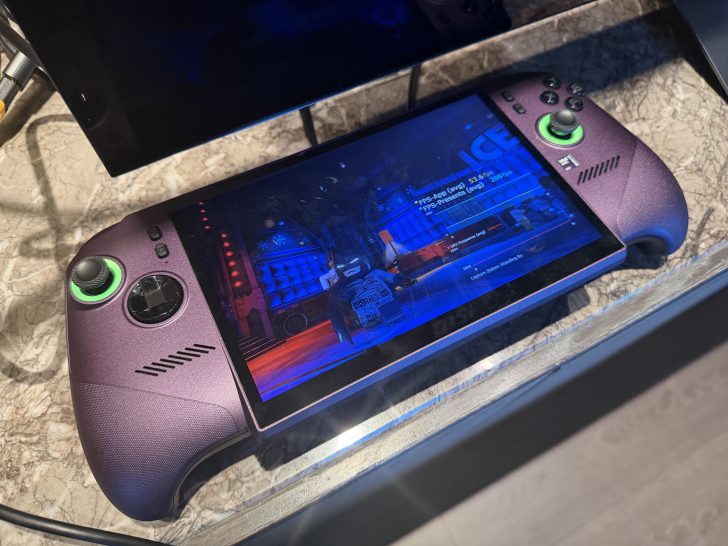 The ROG handheld gaming device displays an in-game scene with performance metrics, including 'FPS-Avg (avg) 53.93', on its screen.