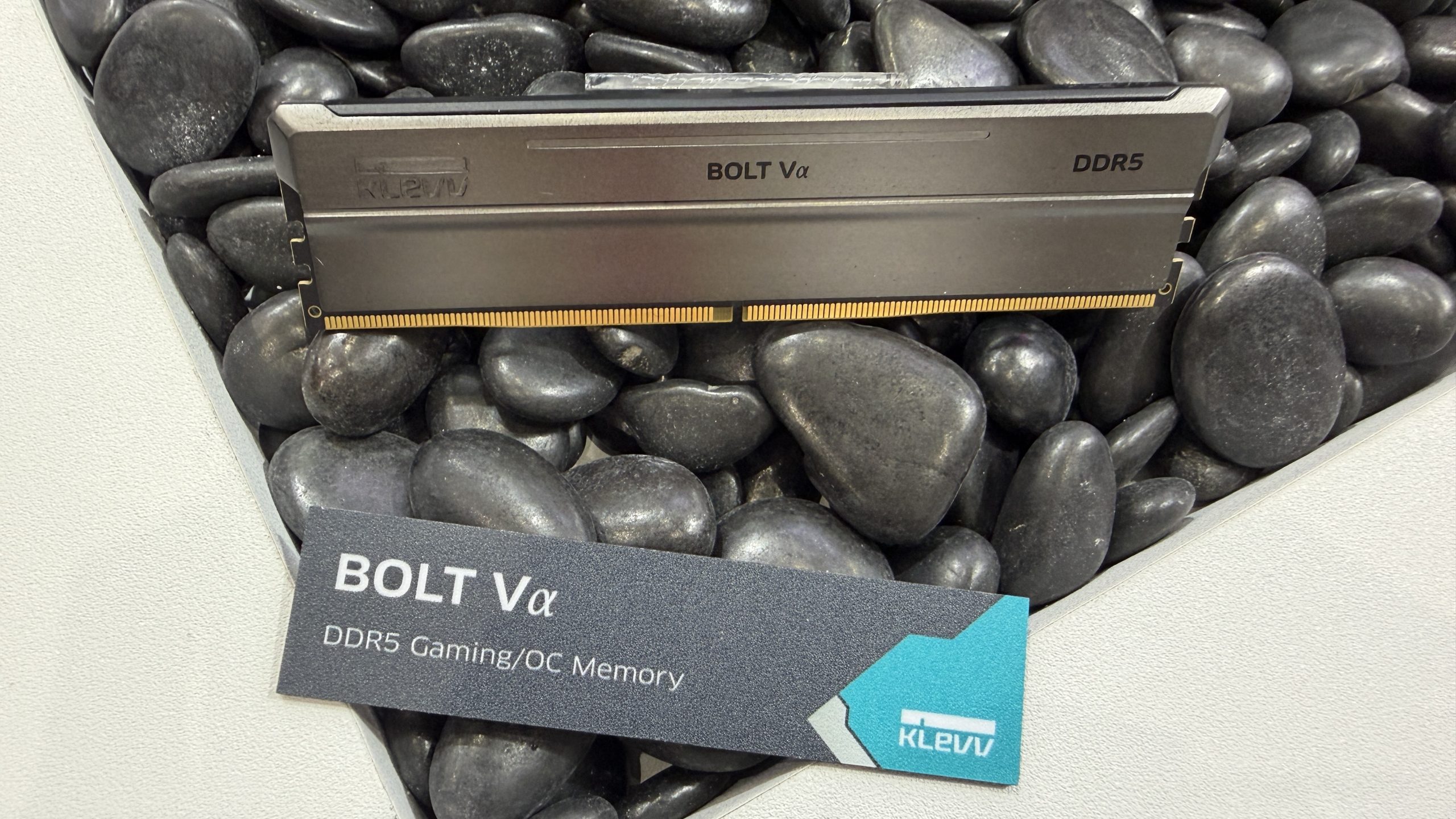 A Klevv BOLT Vα DDR5 RAM module is displayed on a bed of black stones, with a card highlighting it as DDR5 Gaming/OC Memory.