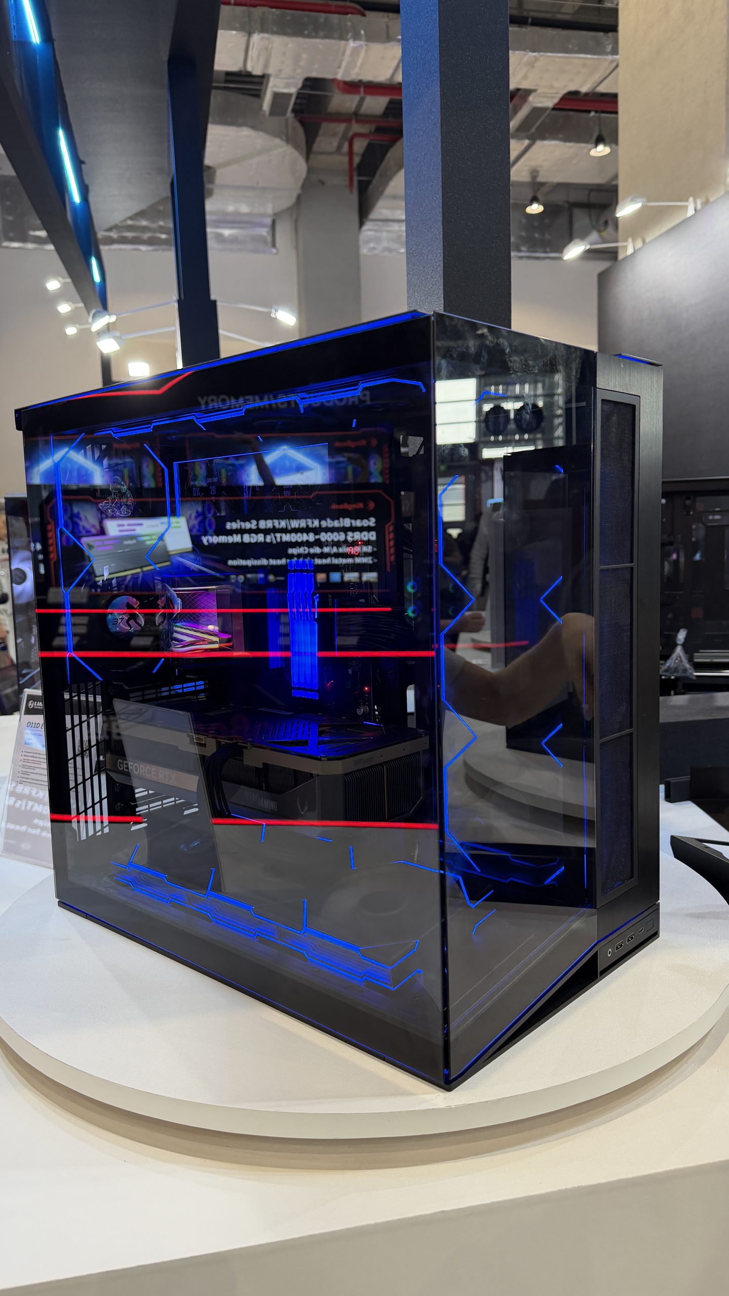 A transparent PC case featuring a GeForce RTX GPU and DDR5-6000MHz RAM, illuminated with blue and red LED lights, is displayed.