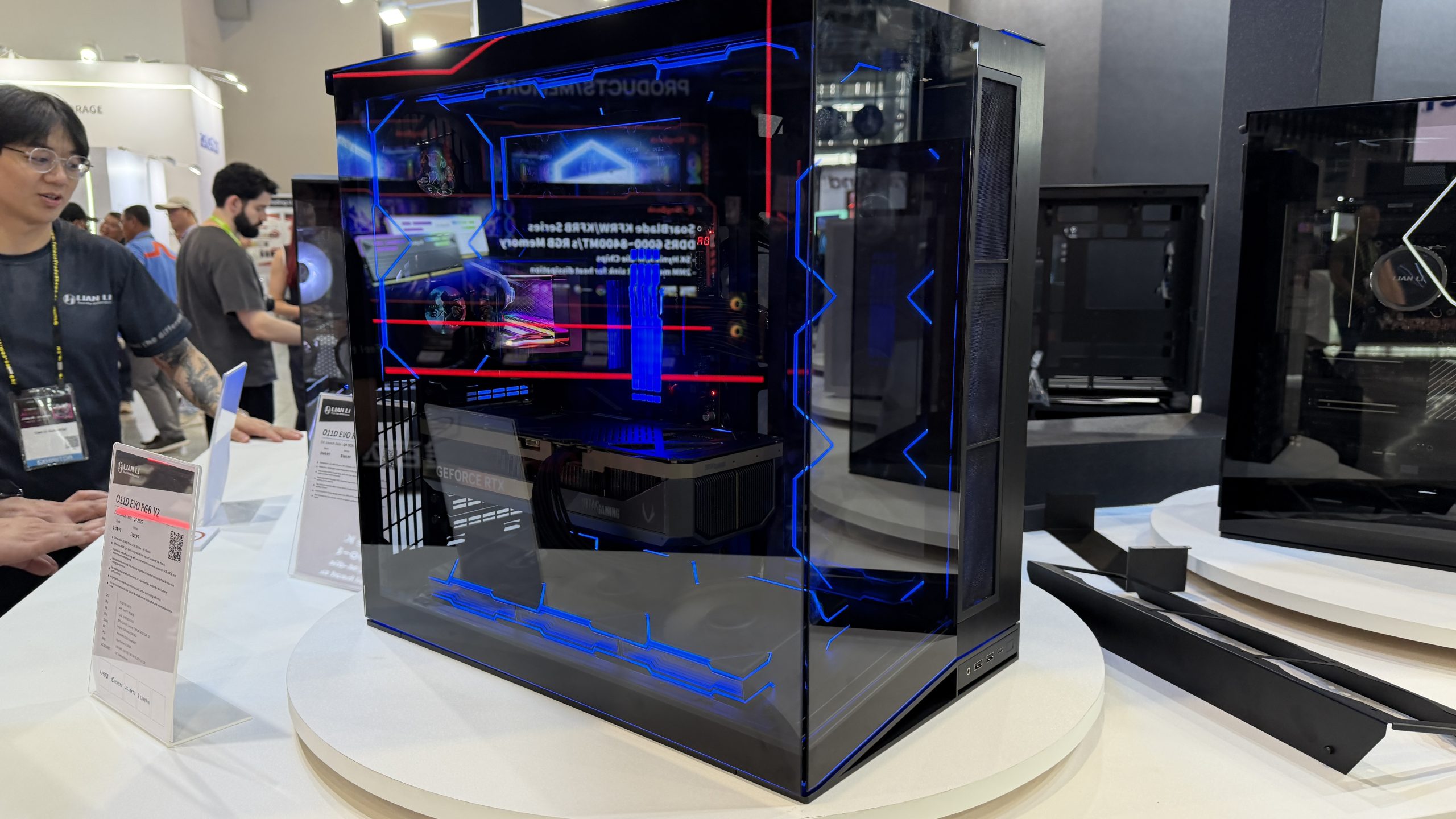A Lian Li O11D EVO RGB V2 gaming case is displayed on a table, featuring a GeForce RTX graphics card visible inside.