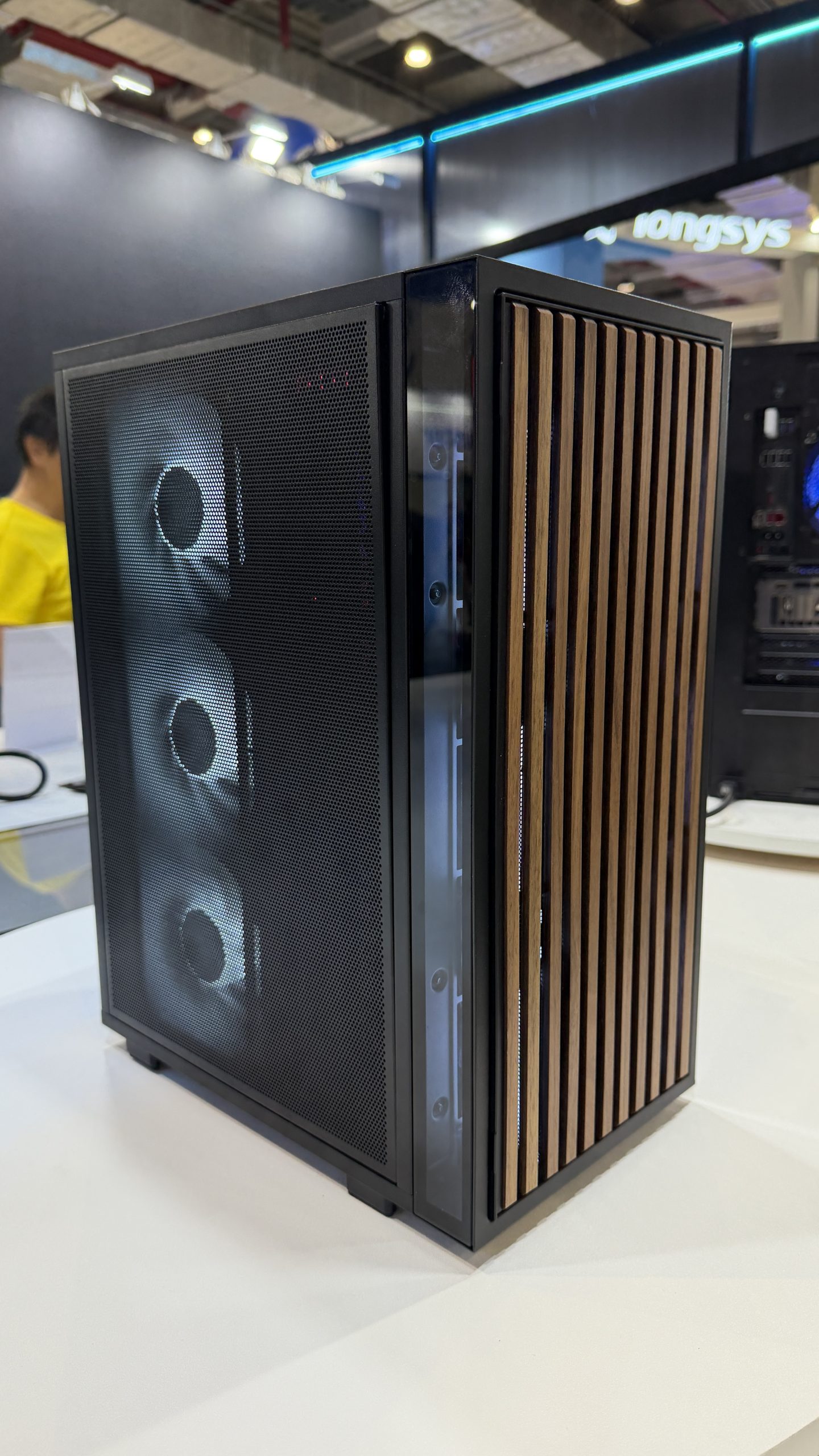 A PC case with a wooden slatted front panel and three visible cooling fans is displayed at a tech booth.