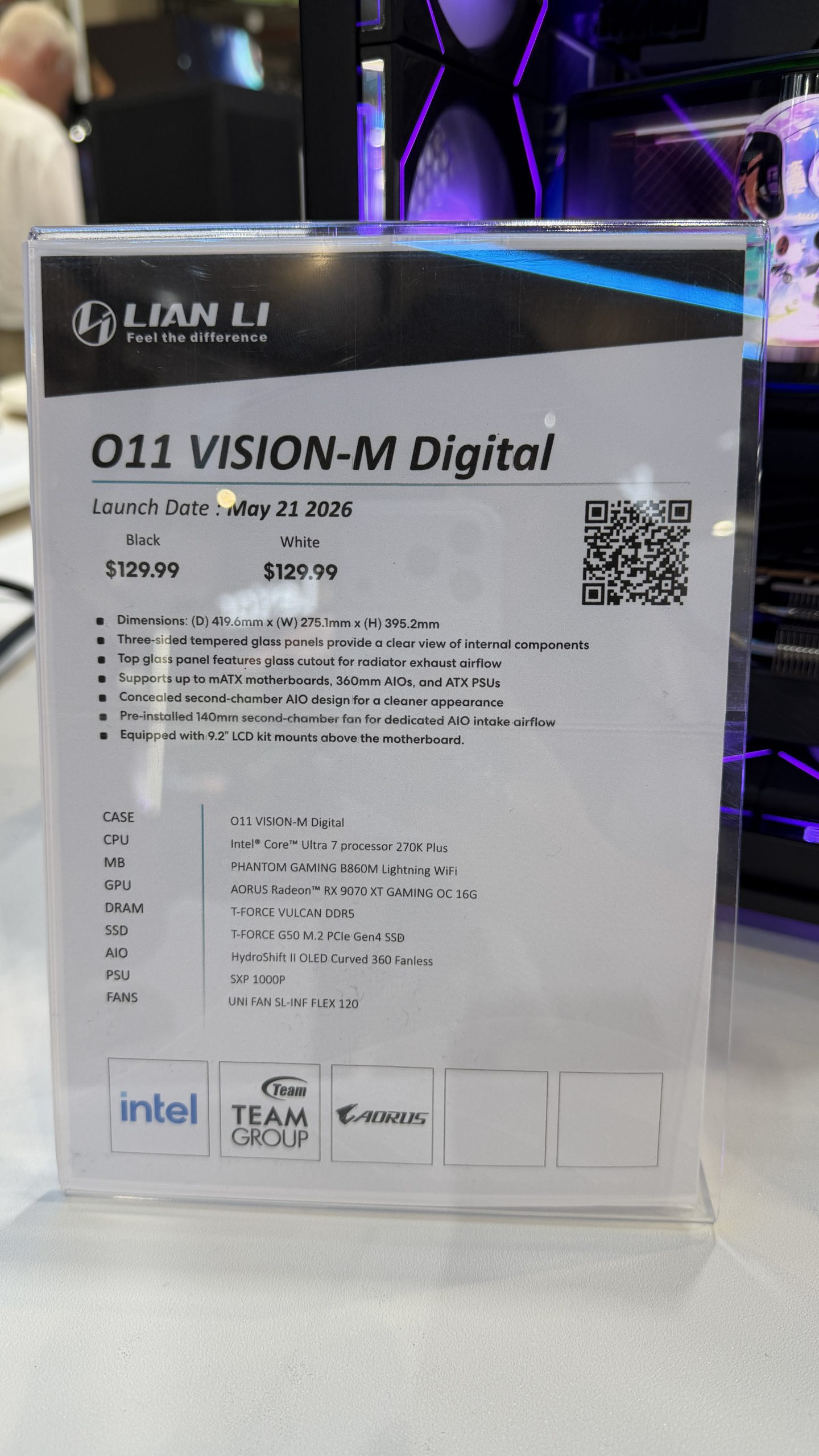 A display sign for the Lian Li O11 VISION-M Digital case shows specifications including an Intel Core Ultra 7 processor 270K Plus, AORUS Radeon RX 9070 XT GAMING OC 16G GPU, and a launch date of May 21, 2026, with pricing at $129.99 for both black and white models.