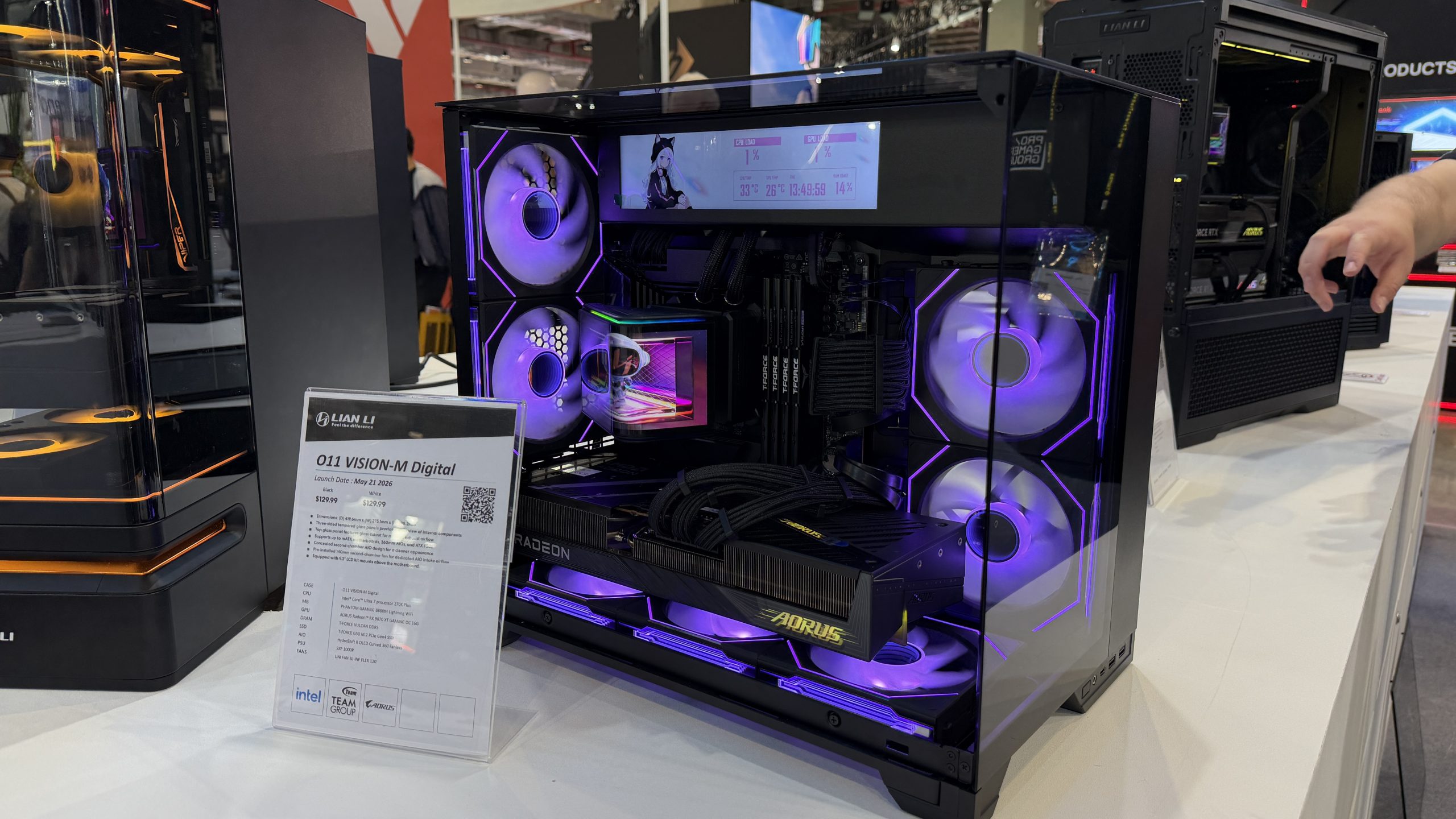 A Lian Li O11 Vision-M Digital PC case is displayed with vibrant purple lighting, featuring a Radeon graphics card and a visible temperature display above.