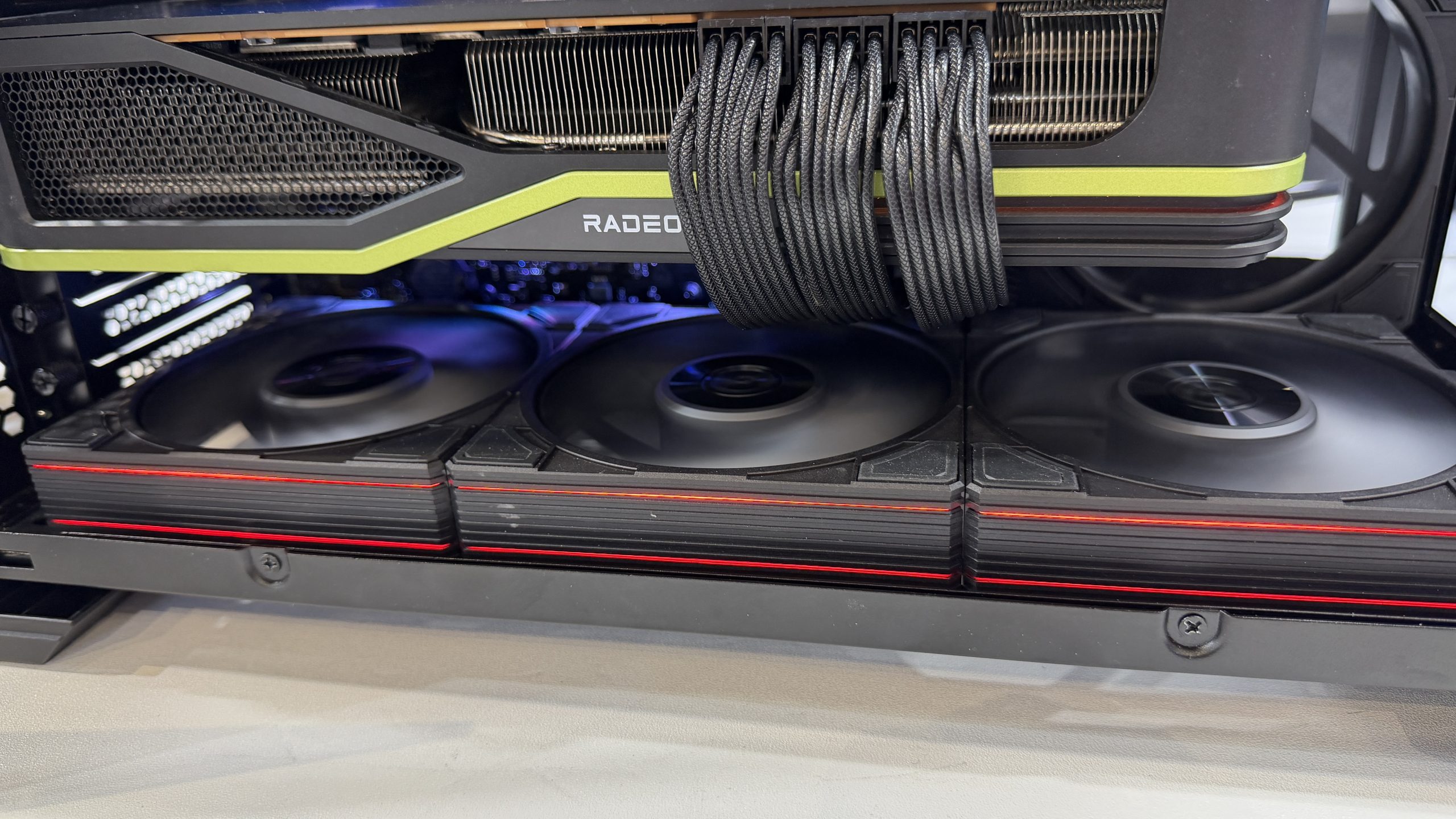 An AMD Radeon graphics card is installed inside a computer case, featuring multiple cooling fans and visible power cables.