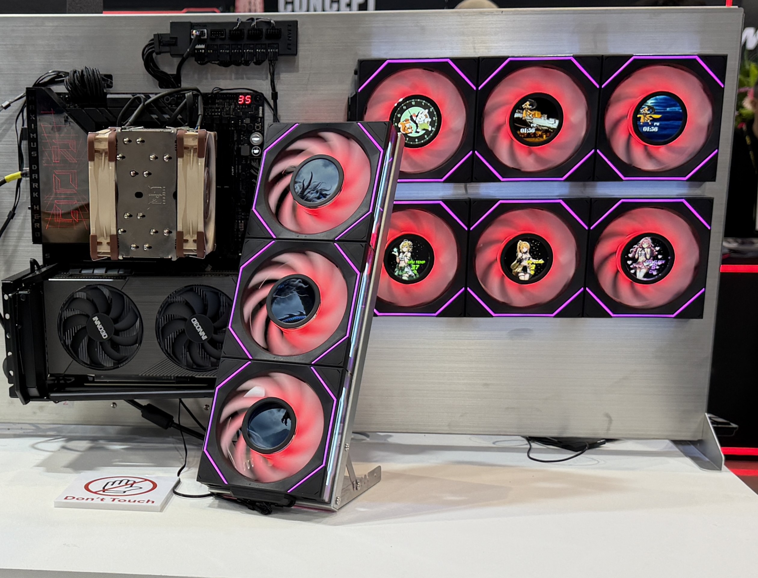 A hardware setup showcasing Noctua and Aorus components with RGB cooling fans, including small circular screens displaying digital characters, is seen on a display marked with 'Don't Touch' signage.