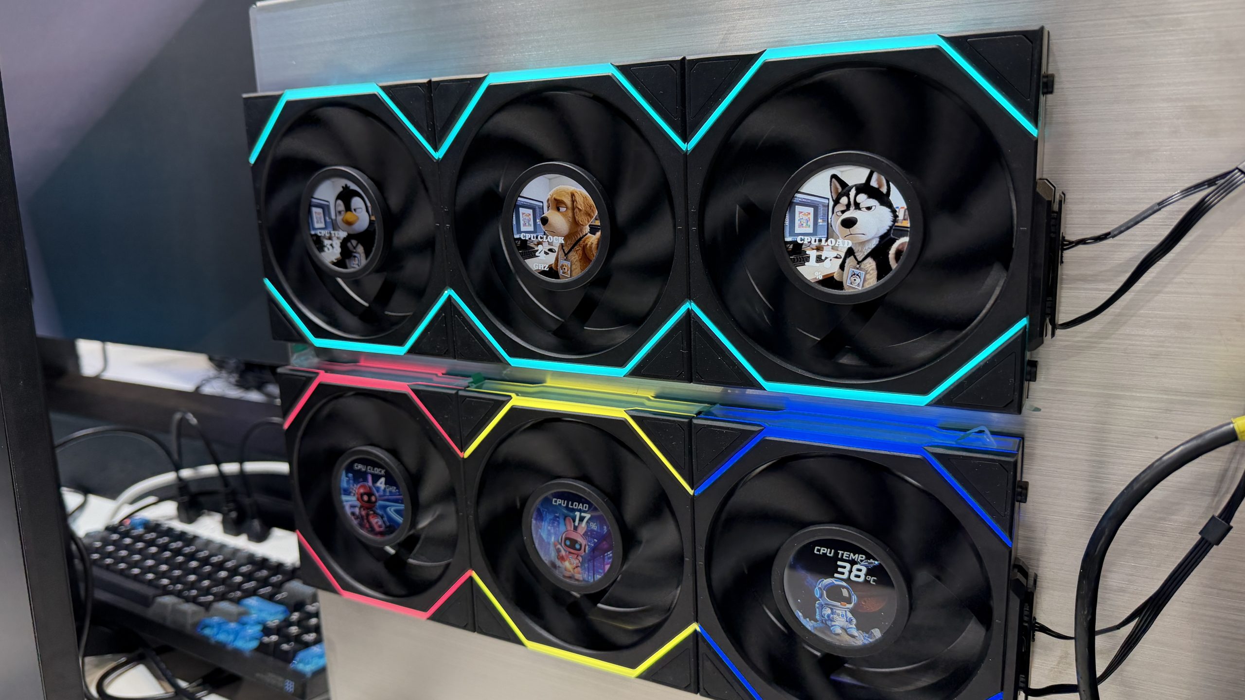 Six illuminated gaming fans are mounted on a wall, each displaying animated characters like a dog and a husky, with indicators such as 'CPU LOAD' and 'CPU TEMP 38°C'.